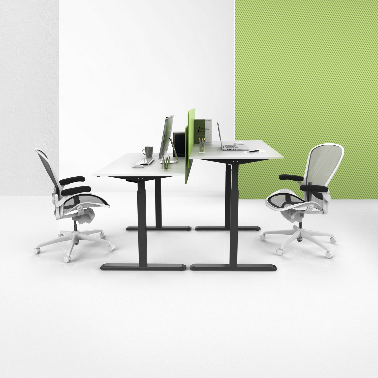 Configuración de oficina con dos escritorios, sillas y divisores. Hay un portátil, un monitor y accesorios en los escritorios. Paredes verdes y blancas.