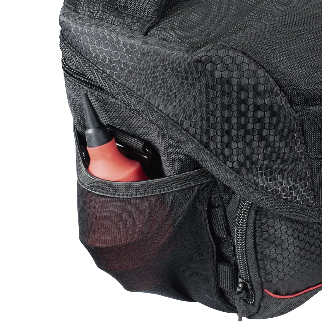 Nahaufnahme einer schwarzen Tasche mit einem rot-schwarzen Gegenstand in einer Seitentasche. Die Tasche hat ein sechseckiges Muster.