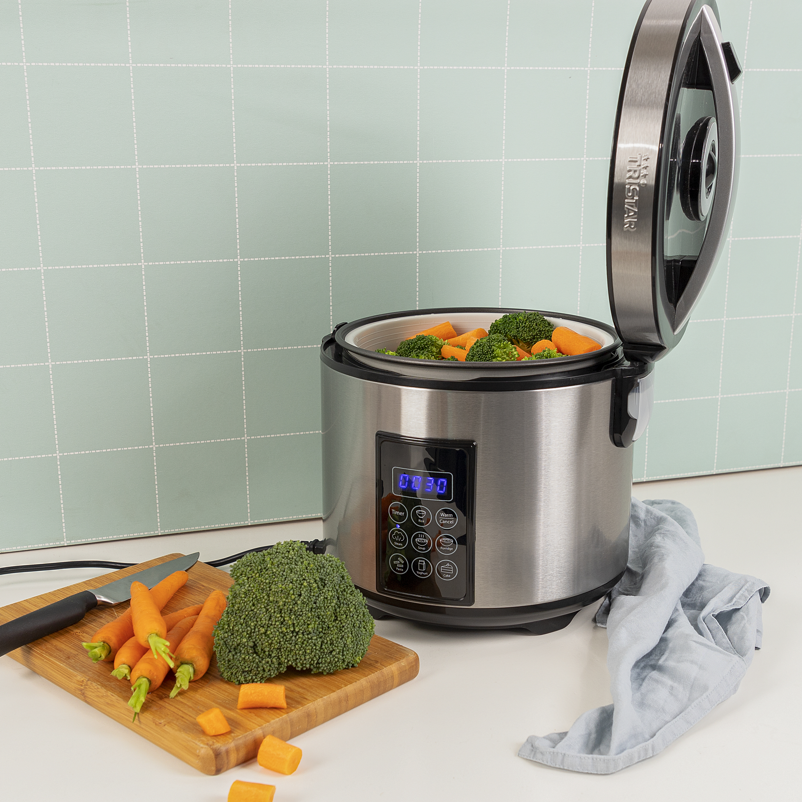 Een steamer met groenten. Wortelen, broccoli en een mes op een houten plank. De deksel is open.
