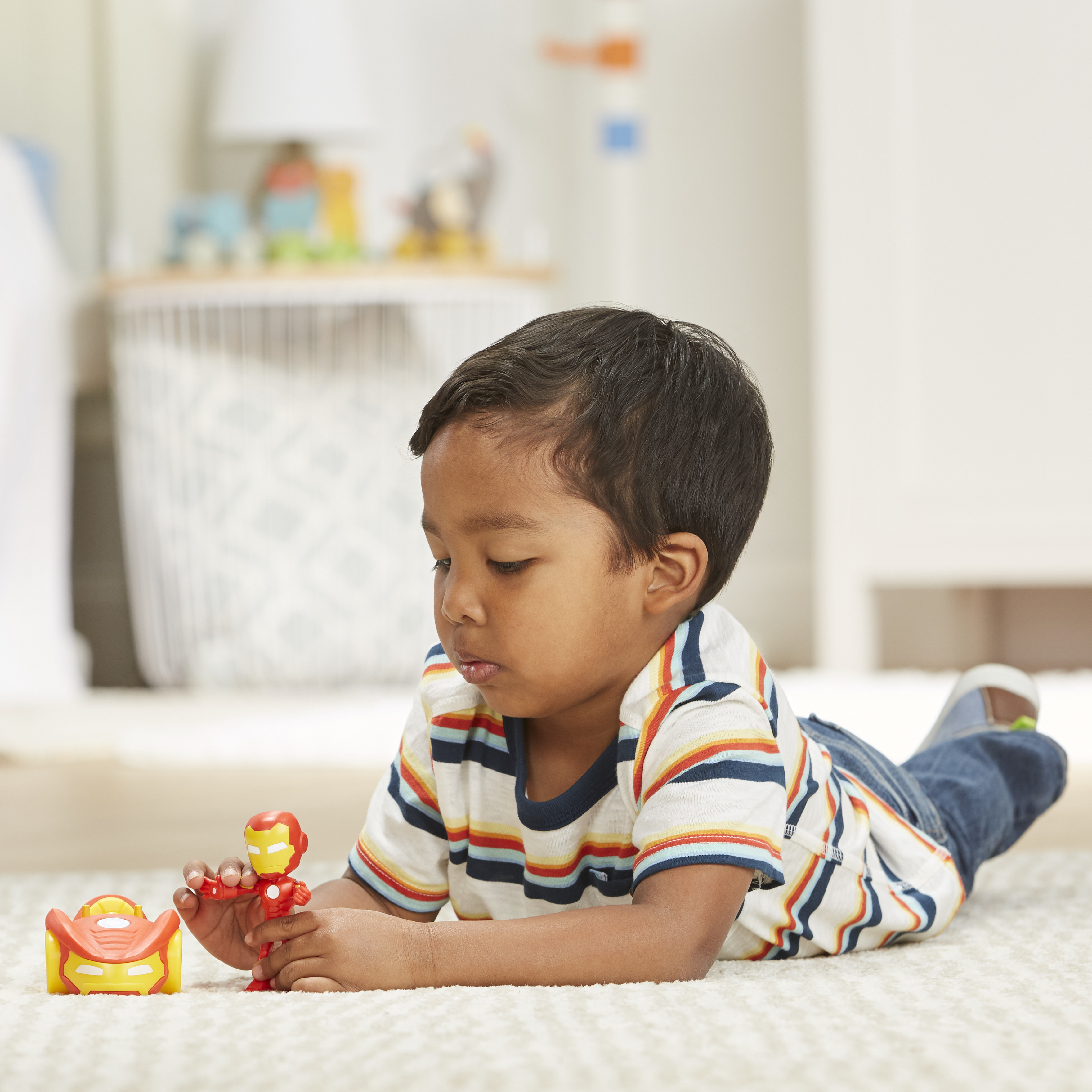 Dziecko leży na dywanie, bawiąc się zabawkami Iron Mana. Jest czerwono-żółty samochód i figurka Iron Mana.