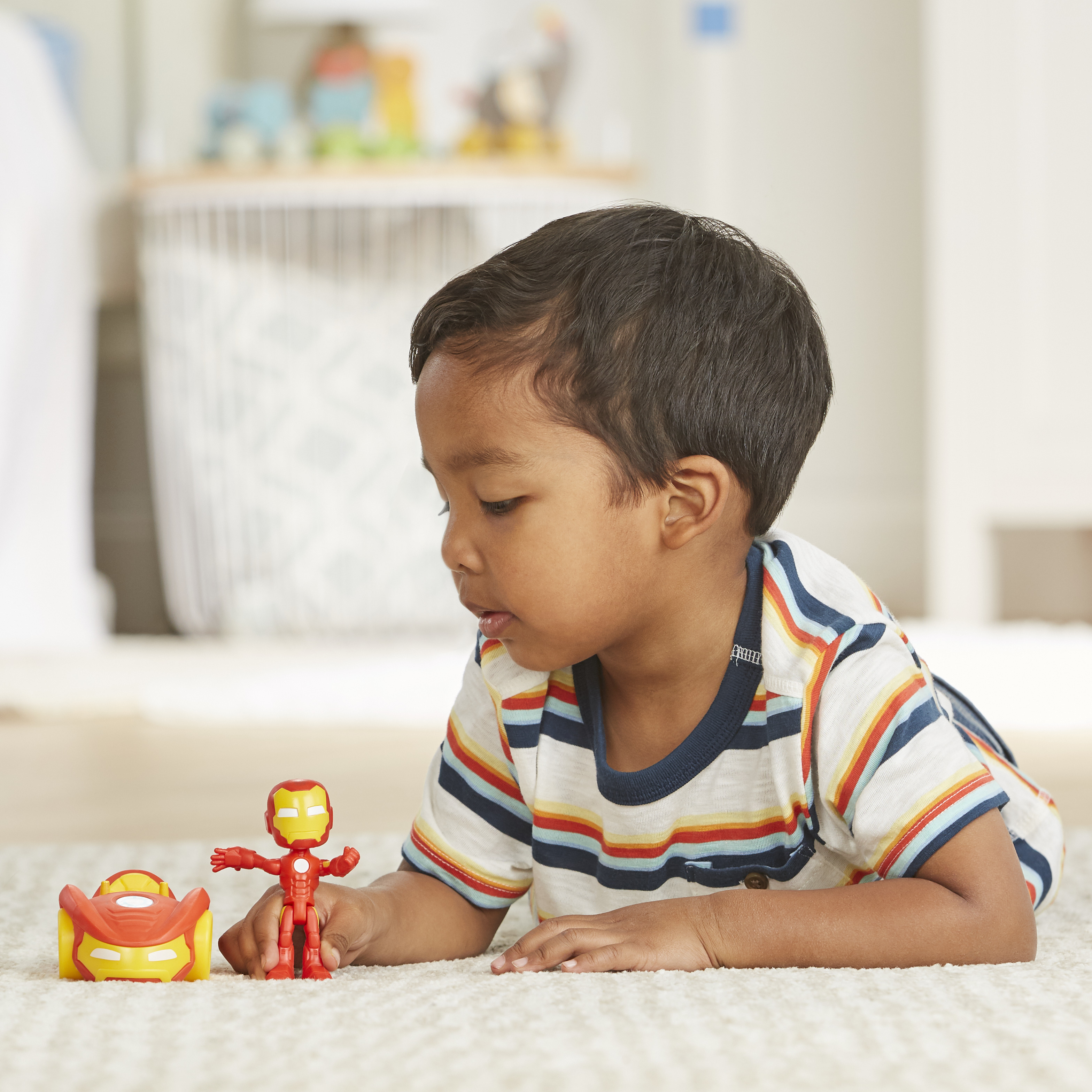 Dziecko leżące na dywanie ogląda zabawki Iron Man. Zabawki obejmują samochód i figurkę.
