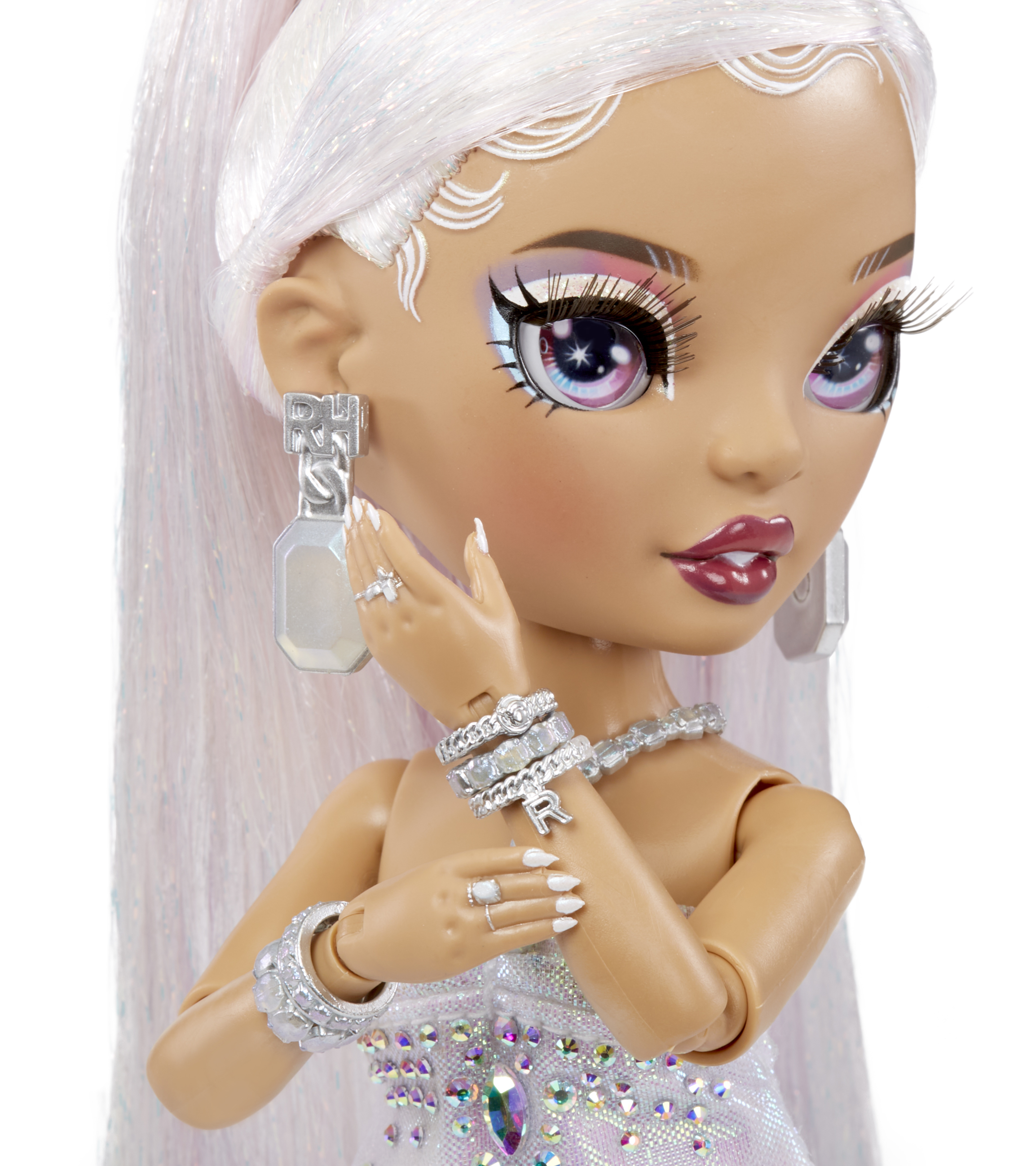 Lalka z białymi włosami, makijażem i biżuterią. Ma na sobie białą sukienkę z kamieniami szlachetnymi i długie białe paznokcie.
