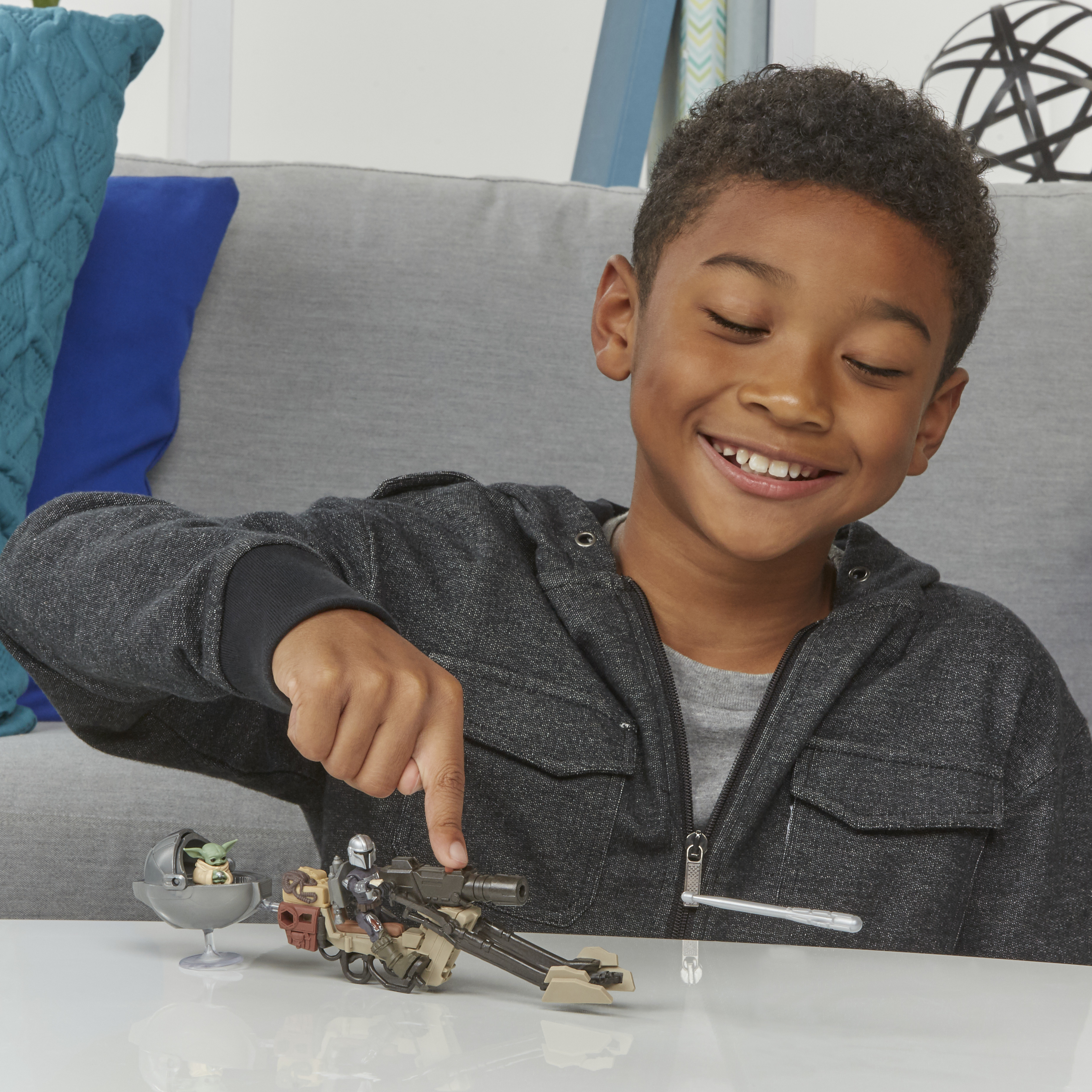Chłopiec wskazuje zestaw zabawek Gwiezdnych Wojen. Zestaw zawiera figurkę Mandalorianina, Grogu i ścigacz.