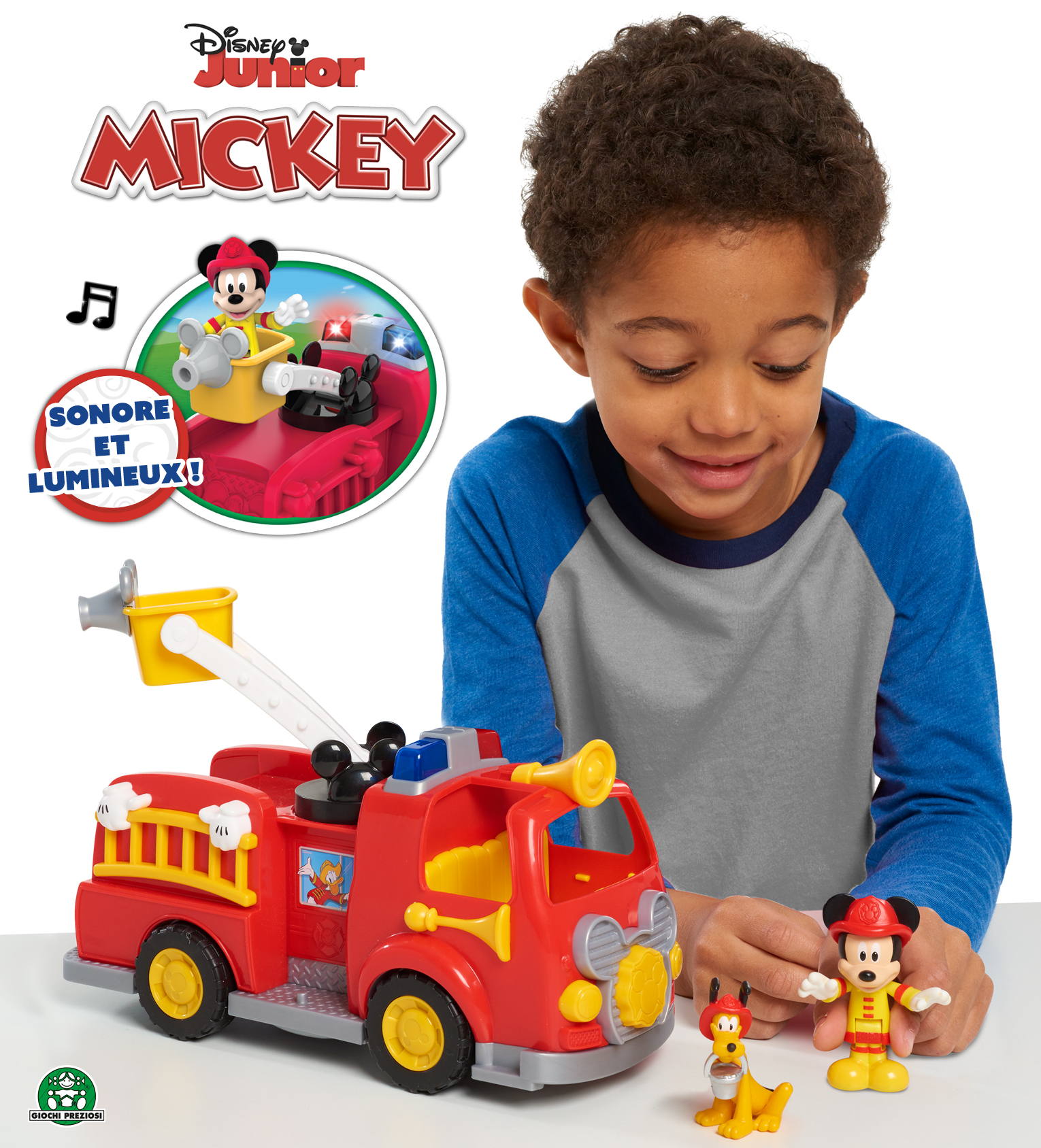 Chłopiec patrzy na zabawkę wozu strażackiego Myszki Miki. Figurki Myszki Miki i Pluto znajdują się obok ciężarówki. Ciężarówka jest czerwona i żółta.