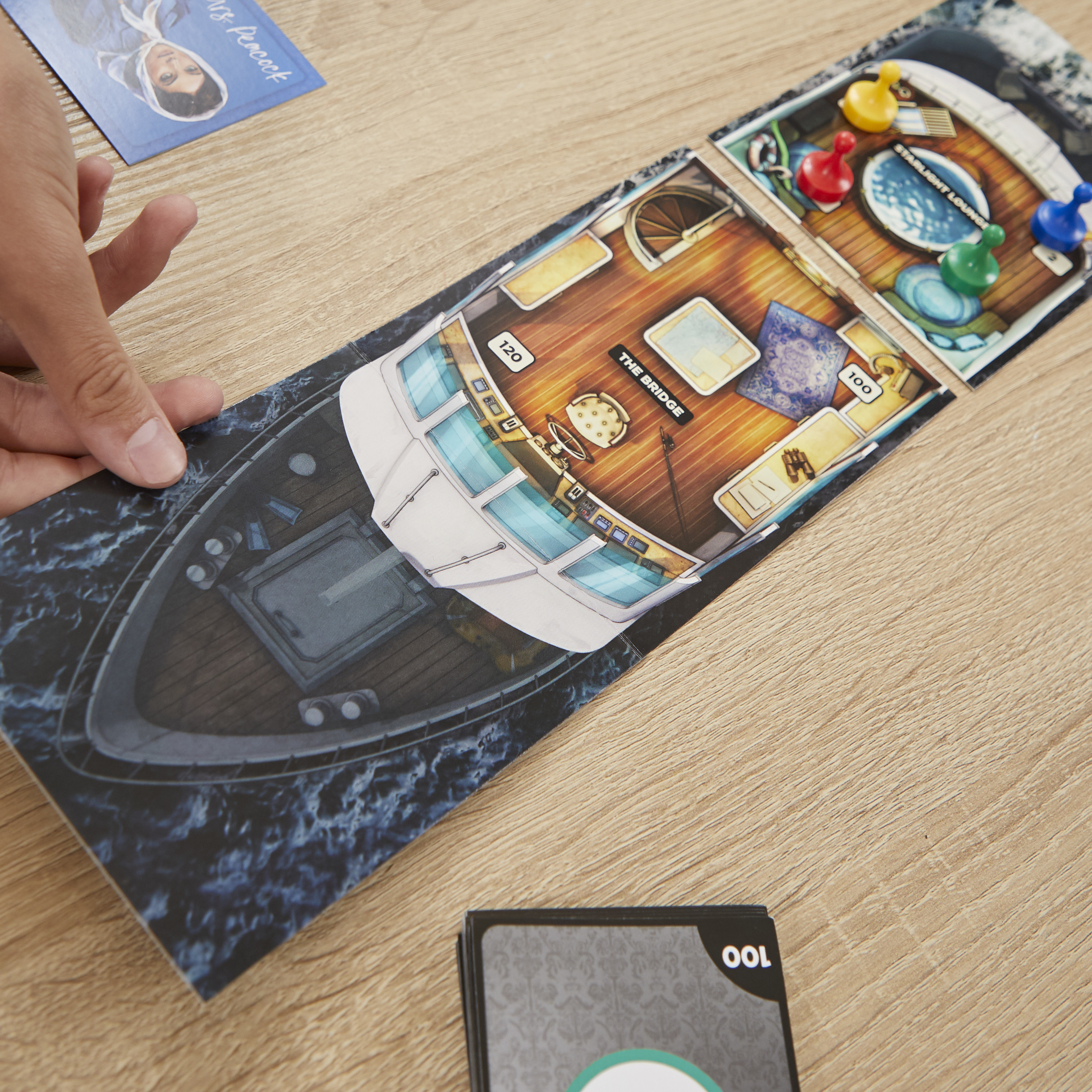 Brettspiel mit Bootslayout, Spielfiguren und Karten. Hand hält einen Bootsabschnitt. Holztisch.