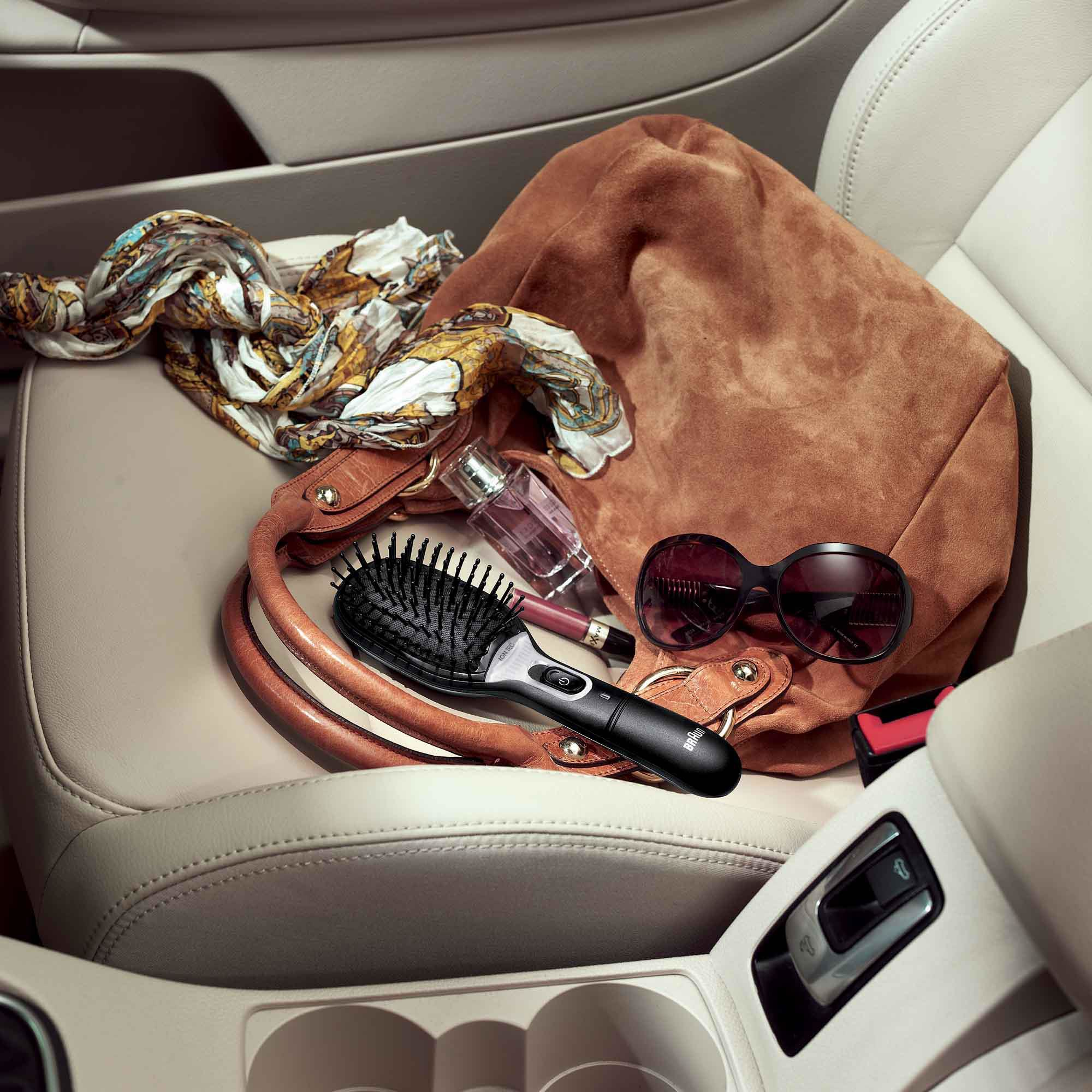 Eine braune Tasche, Sonnenbrille, Bürste, Schal und Parfümflasche in einem Auto. Der Innenraum ist beige.