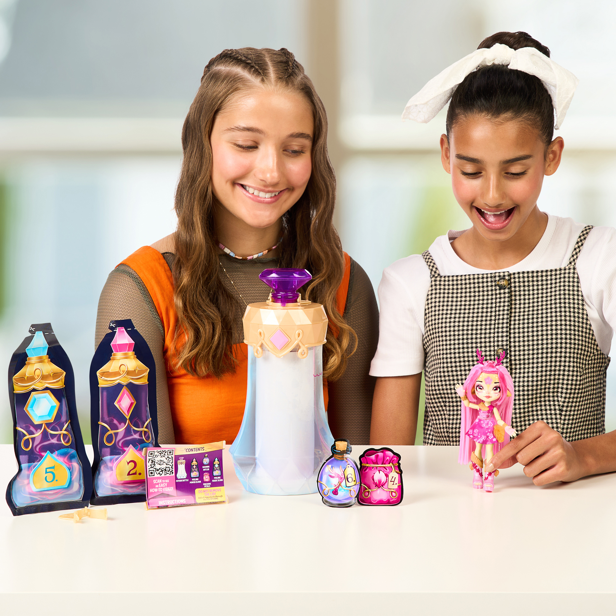 Dwie dziewczyny z zabawkami na stole. Jedna trzyma lalkę. Inne przedmioty to butelki i paczki.