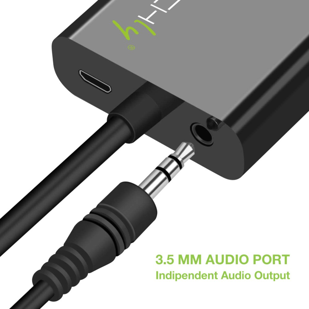 Primer plano de un adaptador de audio negro con un conector jack de 3,5 mm enchufado. El adaptador es gris con puertos y el texto '3,5 MM AUDIO PORT'.