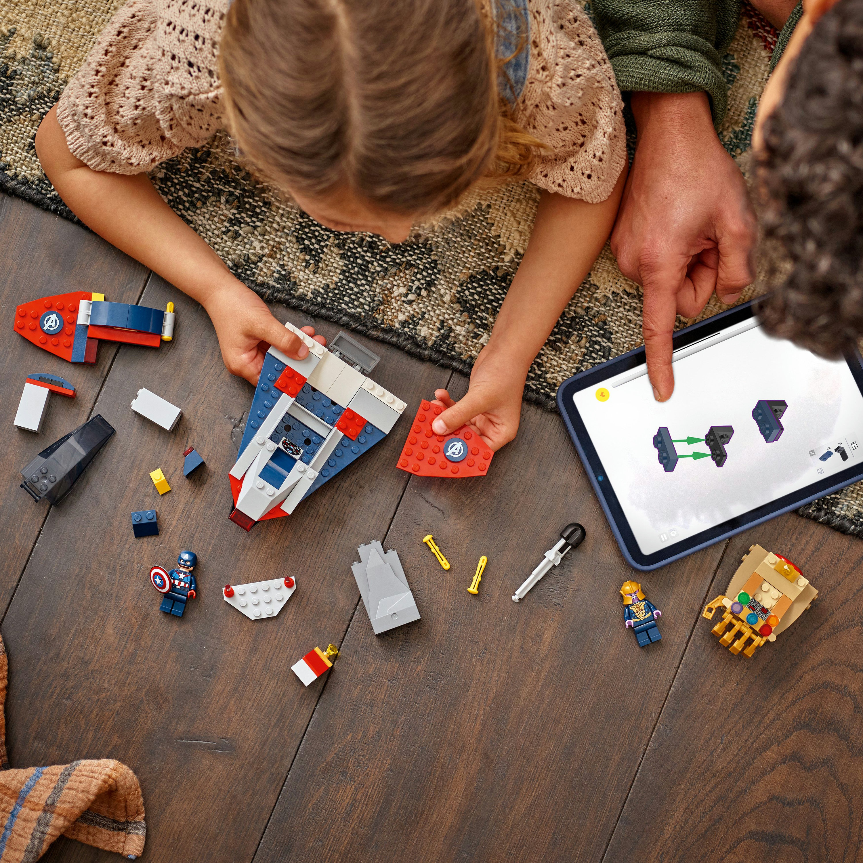 Dziecko i dorosły budują statek Lego. Tablet wyświetla instrukcje. Widoczne są klocki Lego i Kapitan Ameryka.