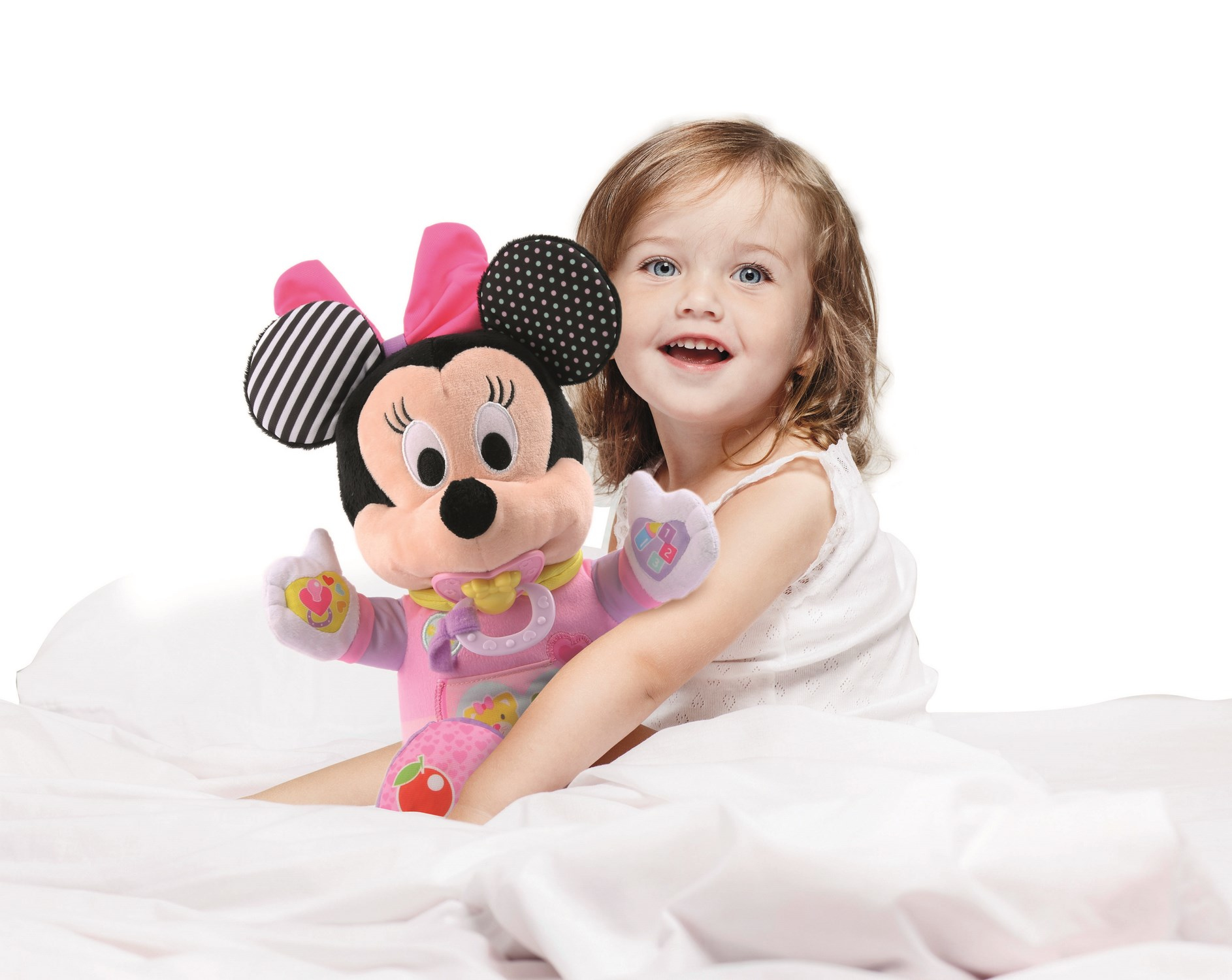 Uśmiechnięte dziecko trzyma lalkę Myszki Minnie na białym łóżku. Lalka jest różowa i czarna. Dziecko ma niebieskie oczy.