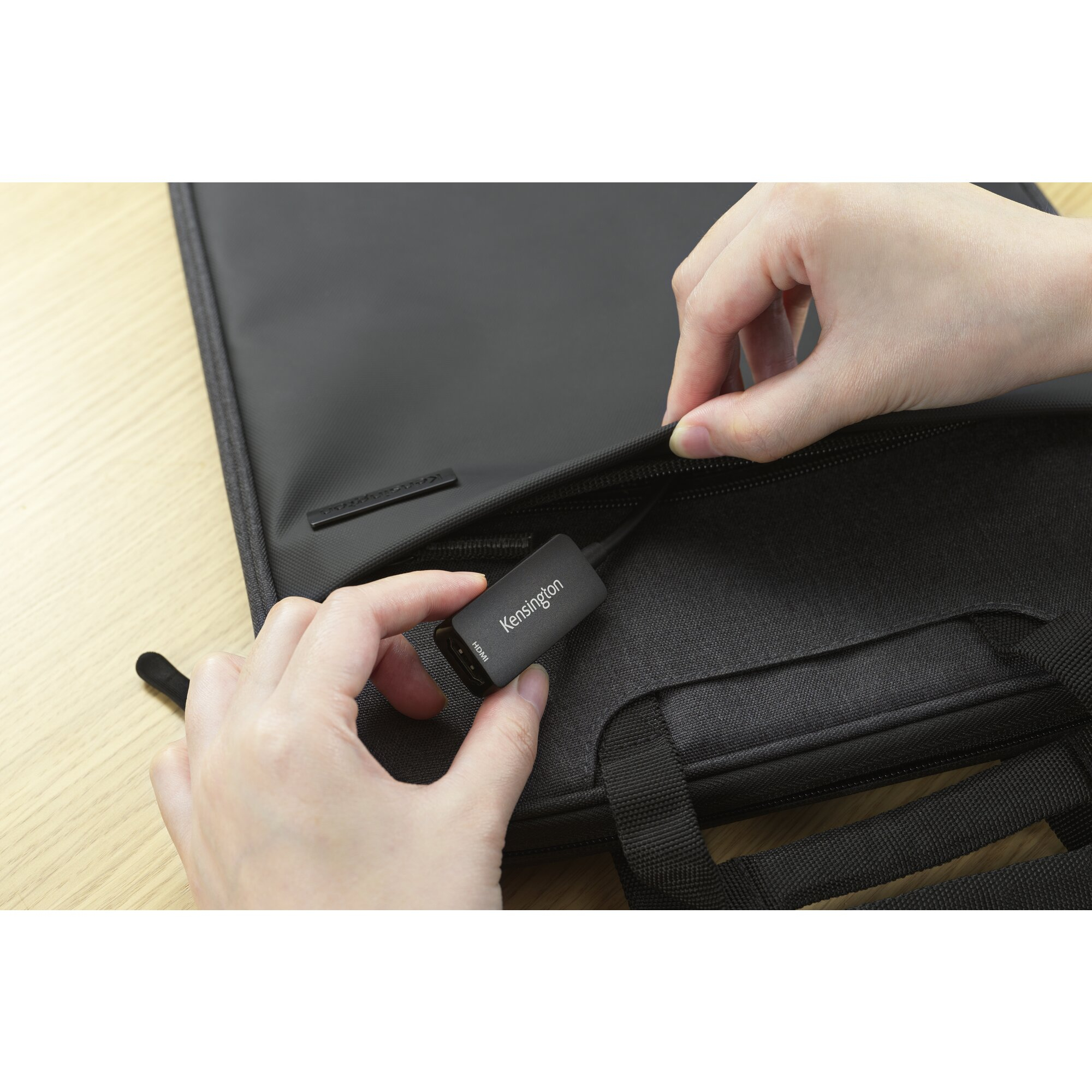 Manos abriendo una bolsa negra para portátil para revelar un adaptador HDMI Kensington.