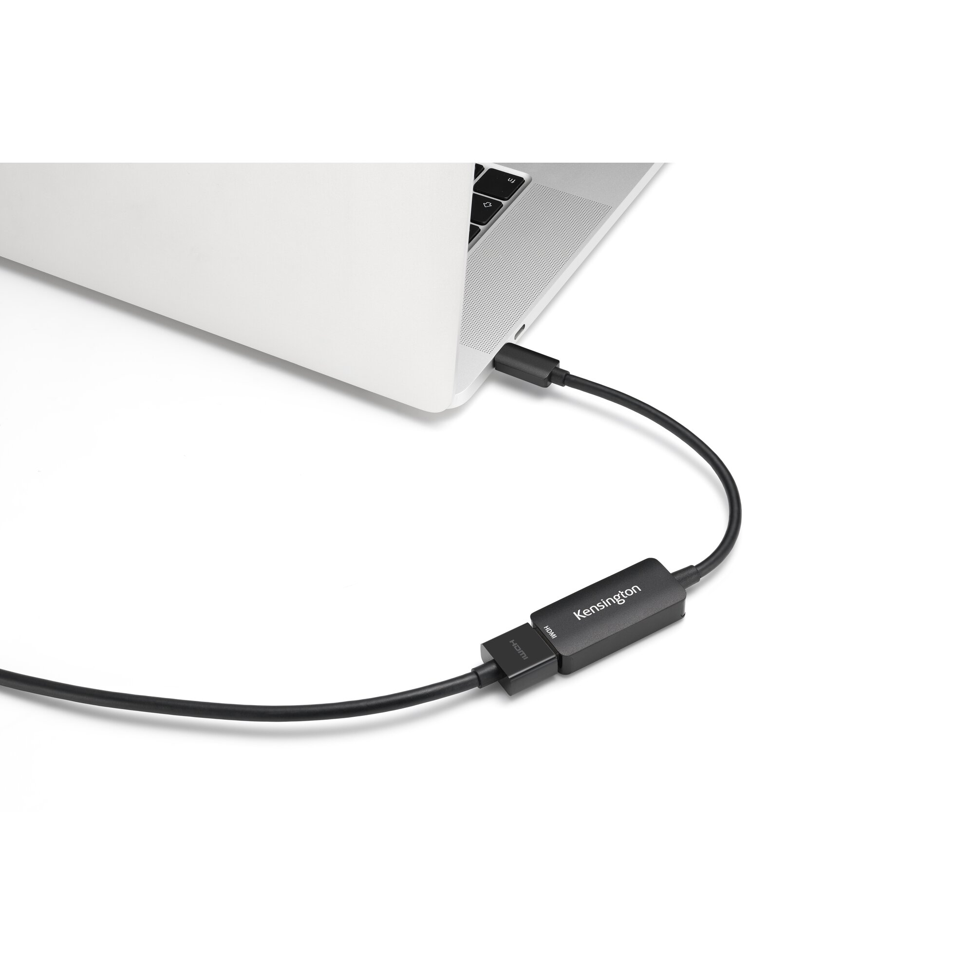 Una laptop está conectada a un adaptador HDMI mediante un cable negro. El adaptador es de Kensington.