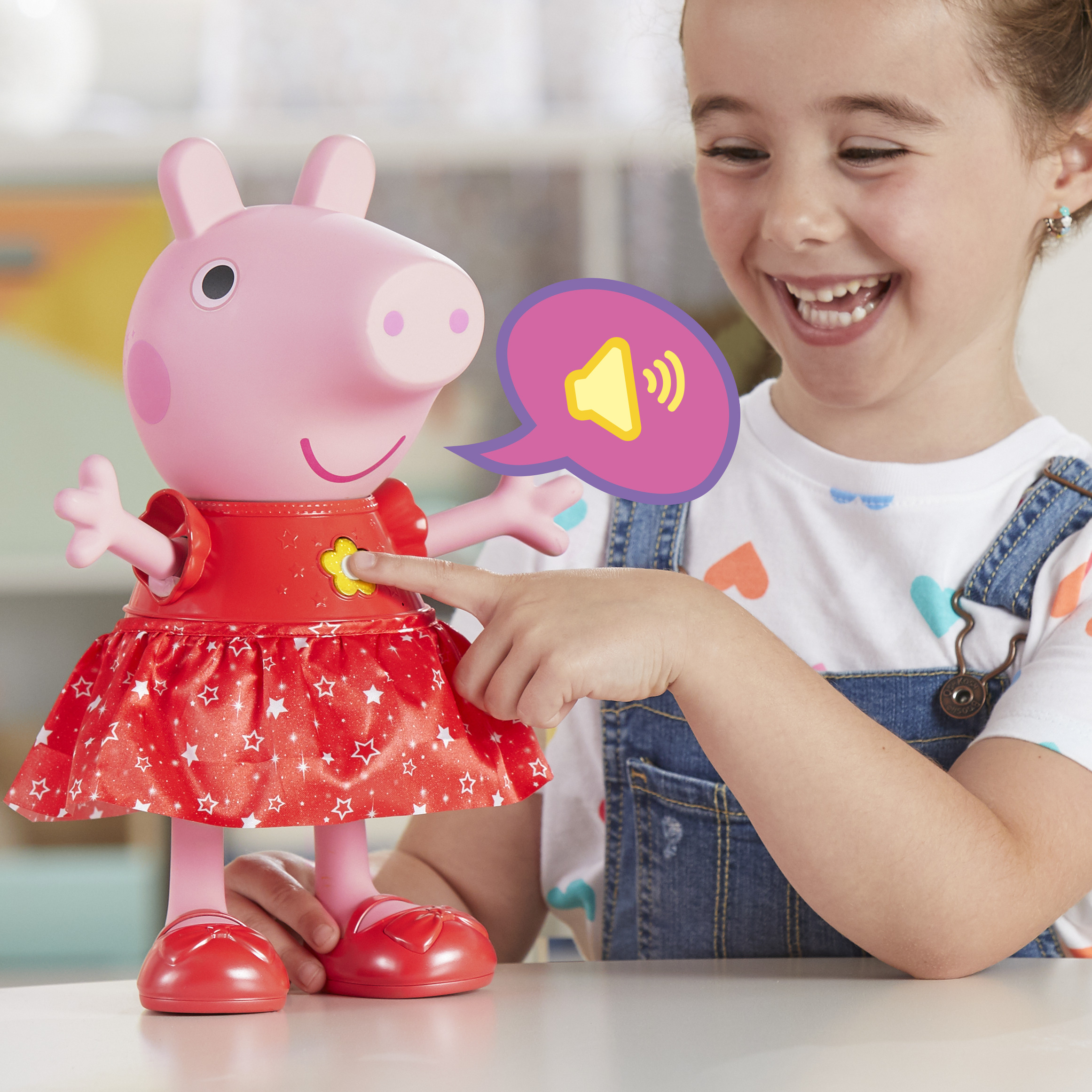 Una niña sonríe, tocando un juguete de Peppa Pig. El juguete lleva un vestido rojo. Un bocadillo con ondas de sonido.