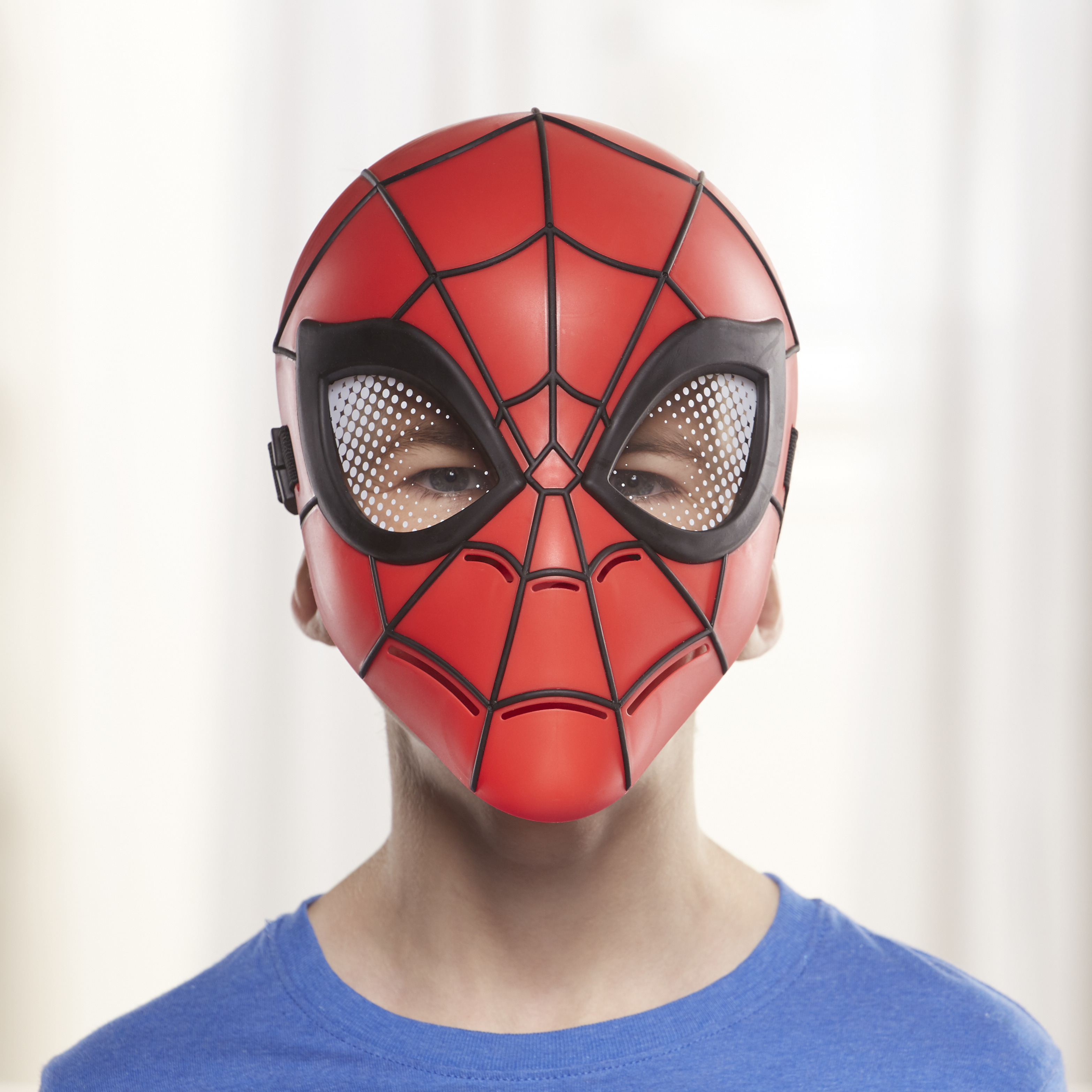Eine Person trägt eine rote Spider-Man-Maske. Schwarze Linien umranden die Maske. Der Hintergrund ist weiß und unscharf.