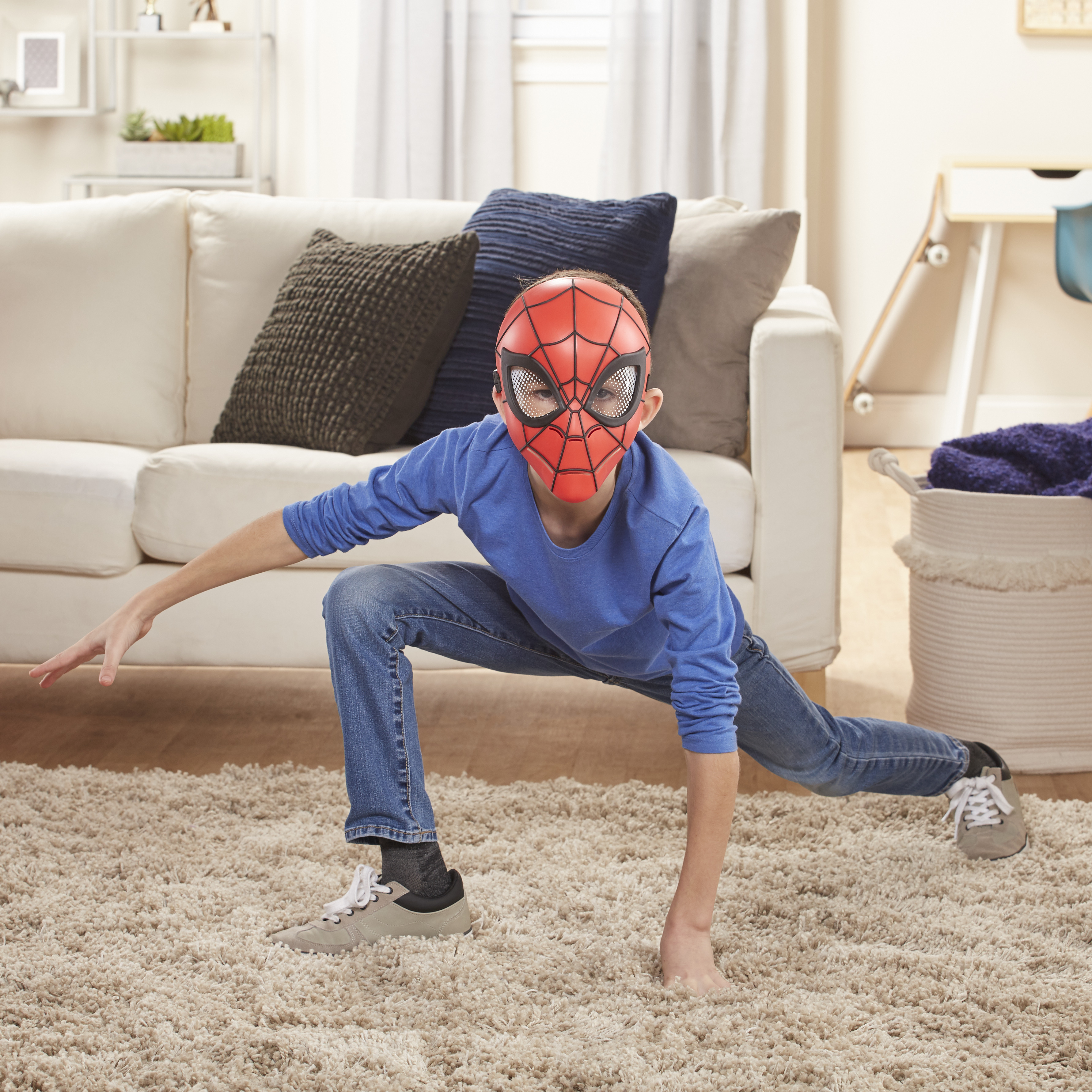 Ein Junge mit Spider-Man-Maske in einer Ausfallschrittposition auf einem Teppich. Eine Couch und ein Korb sind im Hintergrund.