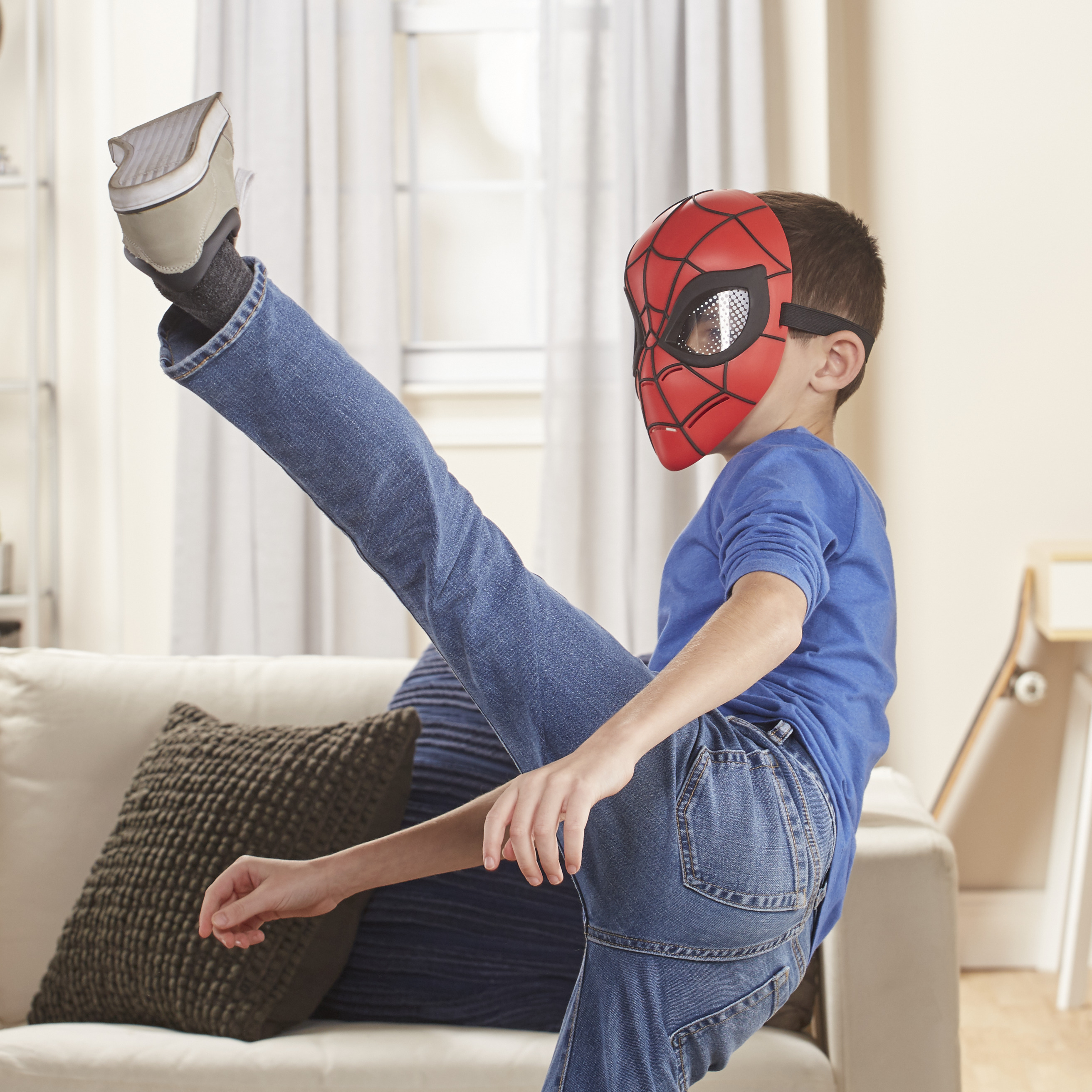Ein Junge mit Spiderman-Maske tritt sein Bein hoch. Er trägt Jeans und ein blaues Hemd.