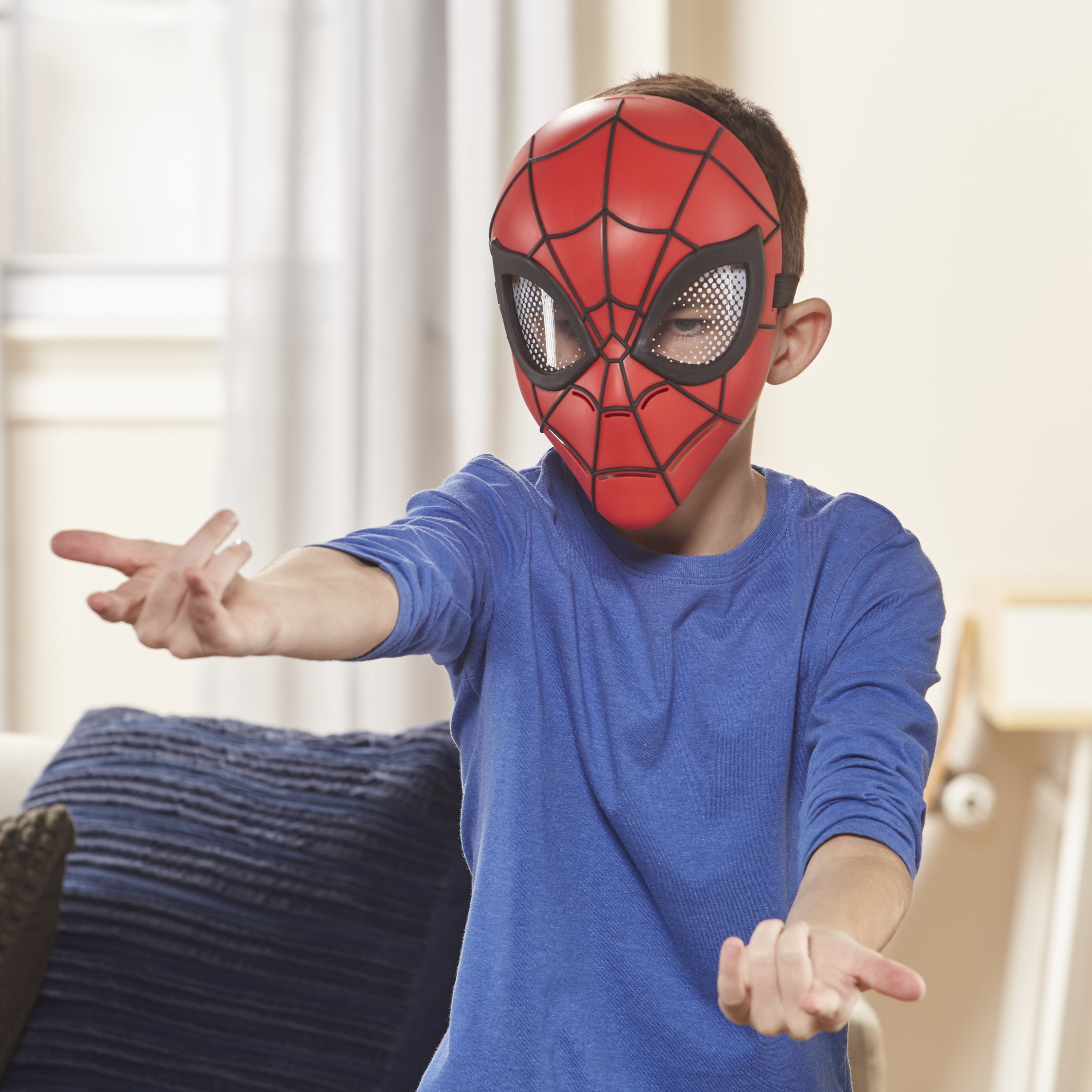 Ein Junge mit einer Spider-Man-Maske und einem blauen Hemd gestikuliert mit den Händen in einem Raum.