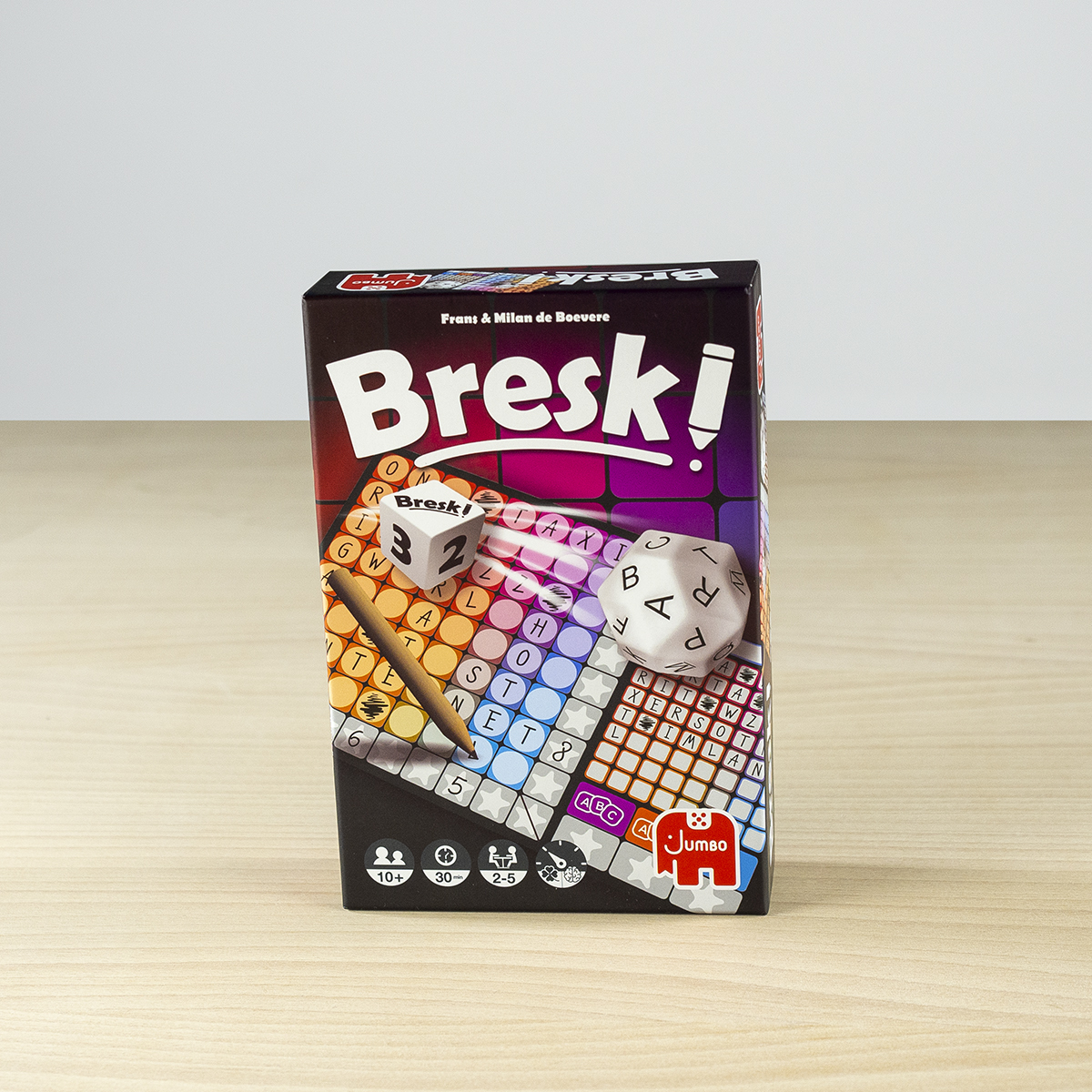 Eine 'Bresk!'-Brettspielbox. Sie hat Würfel, einen Bleistift und ein Gitter aus Buchstaben. Der Hintergrund ist ein Holztisch mit einer weißen Wand.