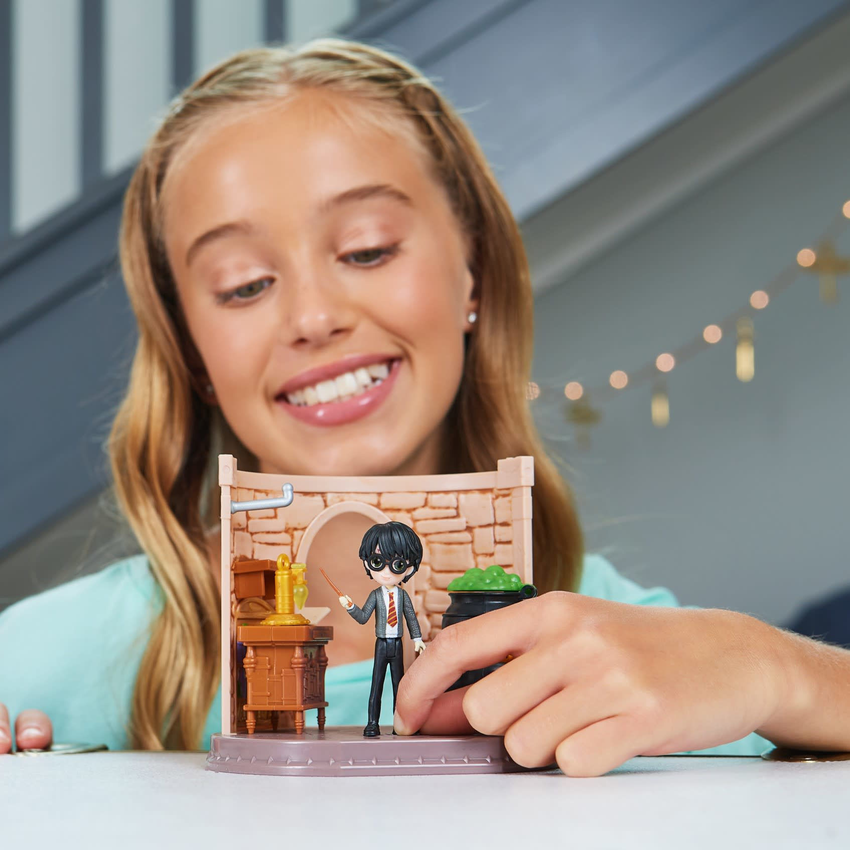 Dziewczyna uśmiecha się do zestawu zabawek Harry'ego Pottera. Zestaw zawiera figurkę Harrego, kociołek i ceglaną ścianę.