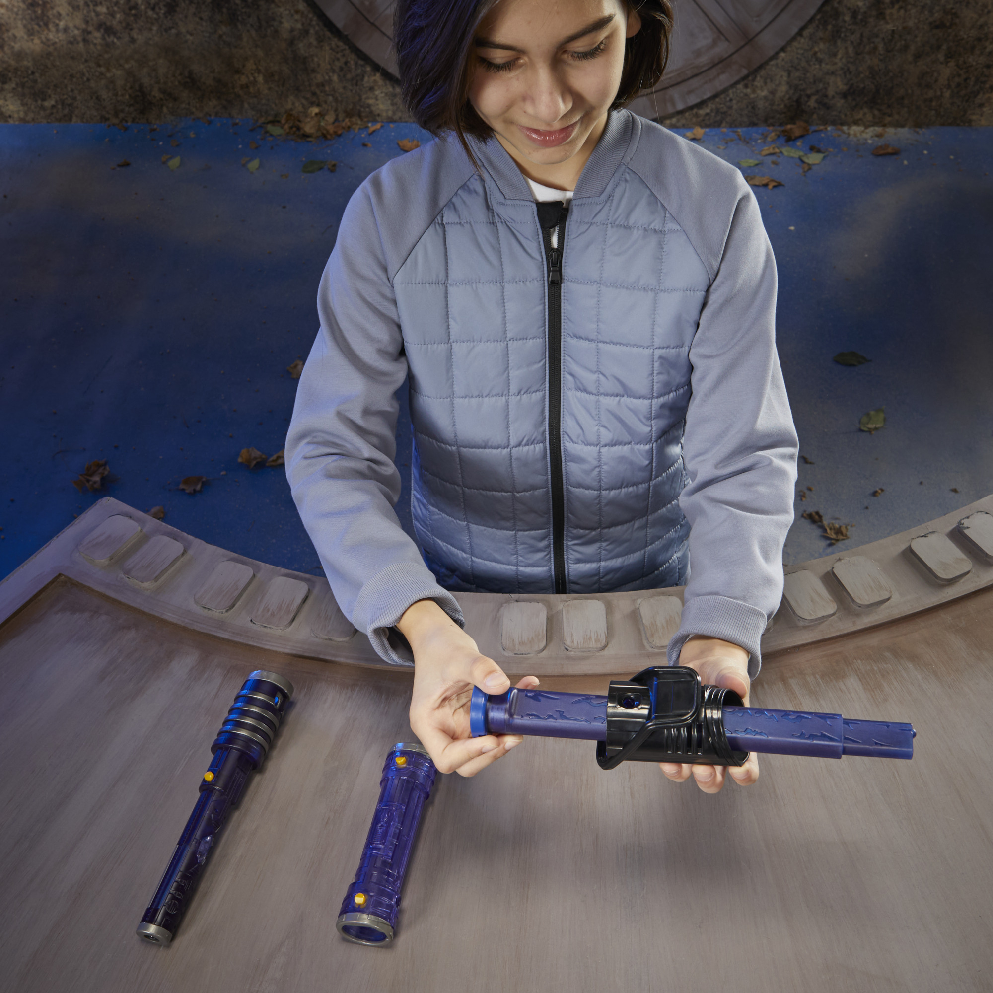 Osoba składająca niebieską zabawkę miecza świetlnego. Na stole widać dwa zdemontowane i jeden złożony miecz świetlny.