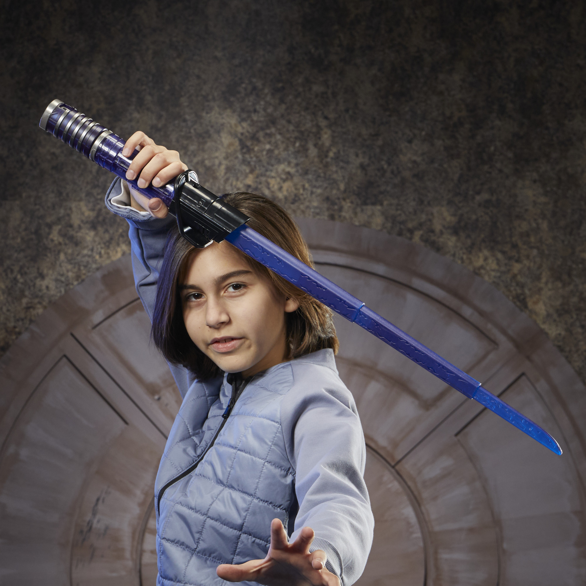 Dziewczyna trzyma niebieski miecz świetlny, pozując z nim. Ma na sobie niebieską kurtkę na brązowym tle.