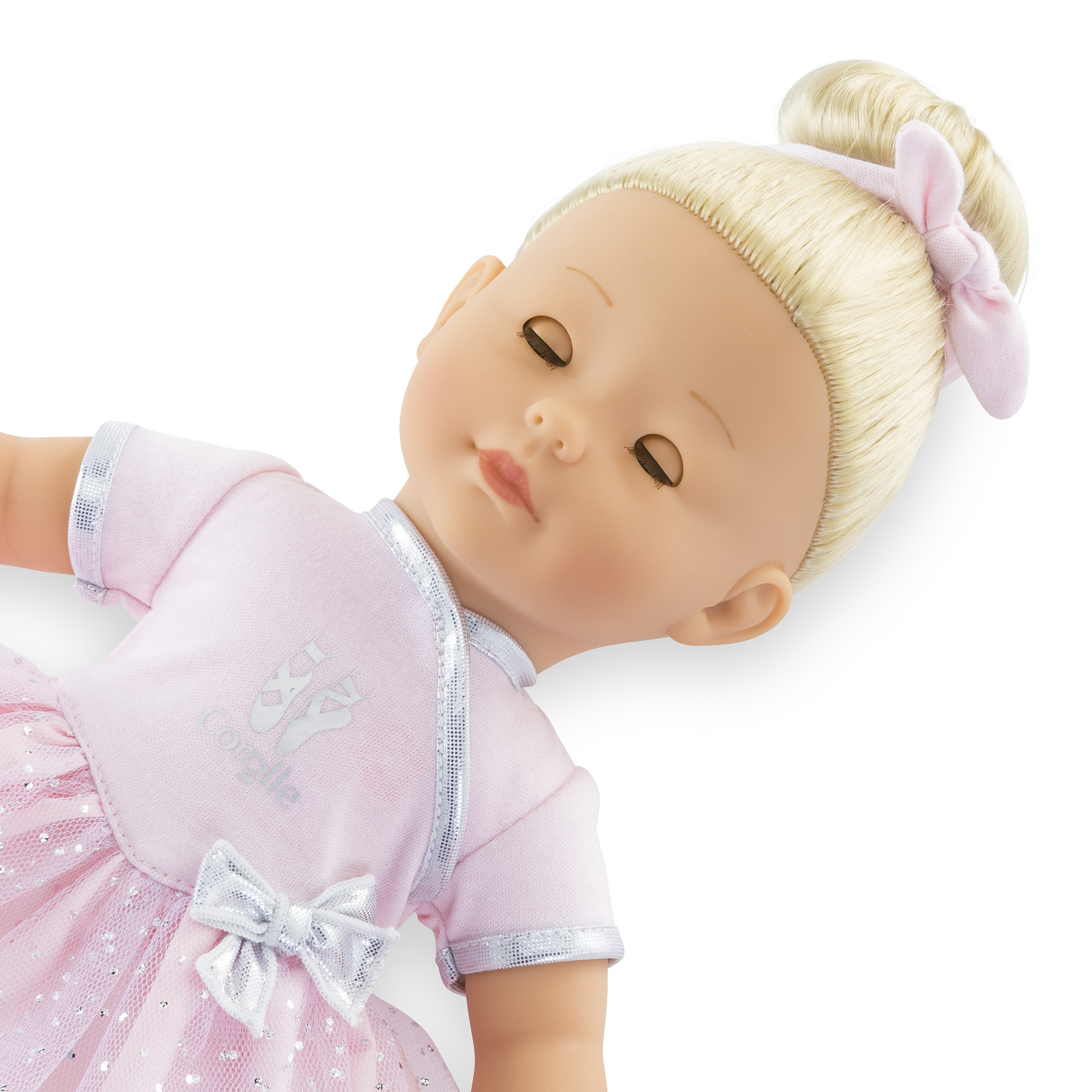 Eine Puppe mit geschlossenen Augen, blonden Haaren in einem Dutt mit einer rosa Schleife. Sie trägt ein rosa Ballettoutfit mit silbernen Akzenten.