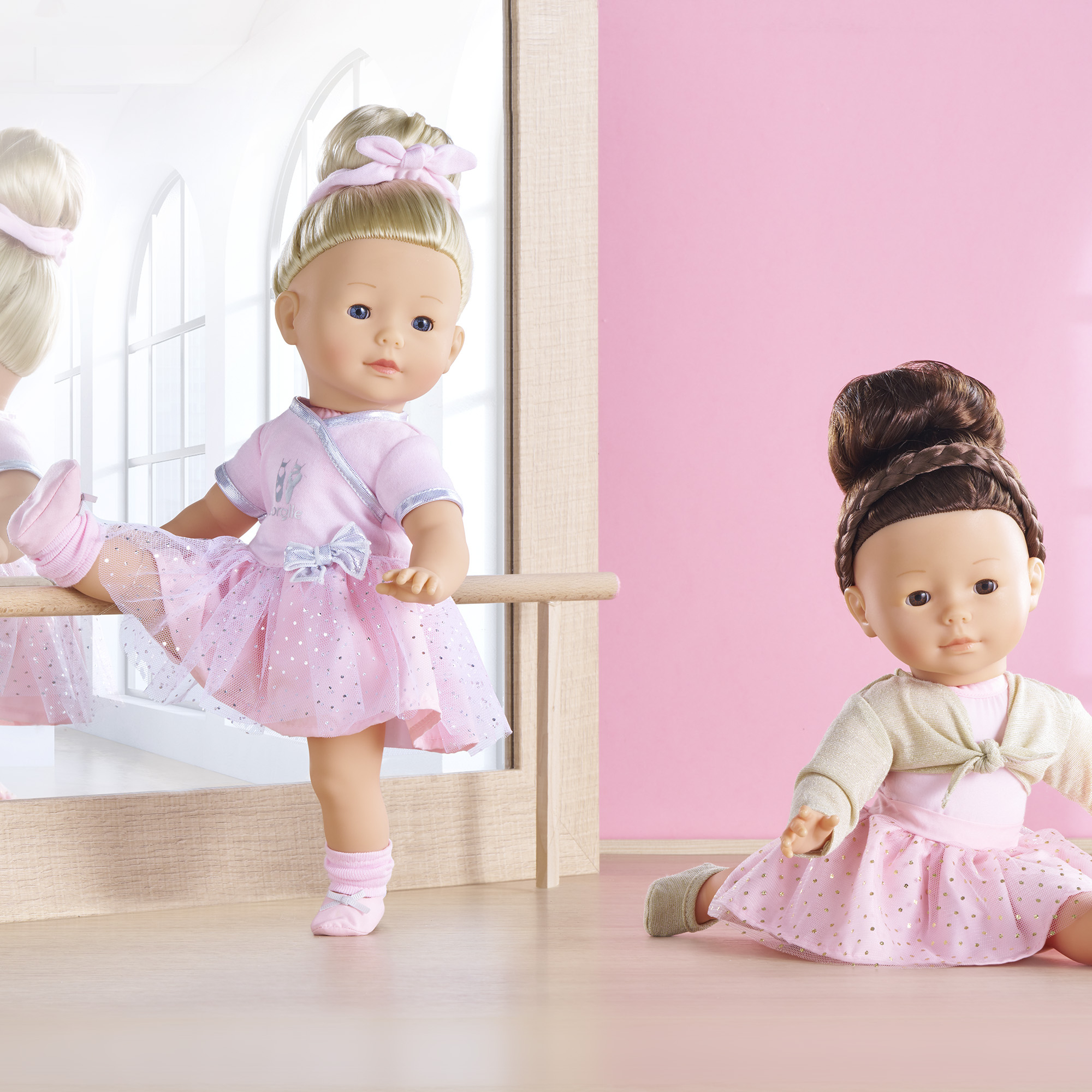 Zwei Puppen in rosa Ballettkleidung. Eine steht an einer Stange, die andere sitzt. Rosa Hintergrund.