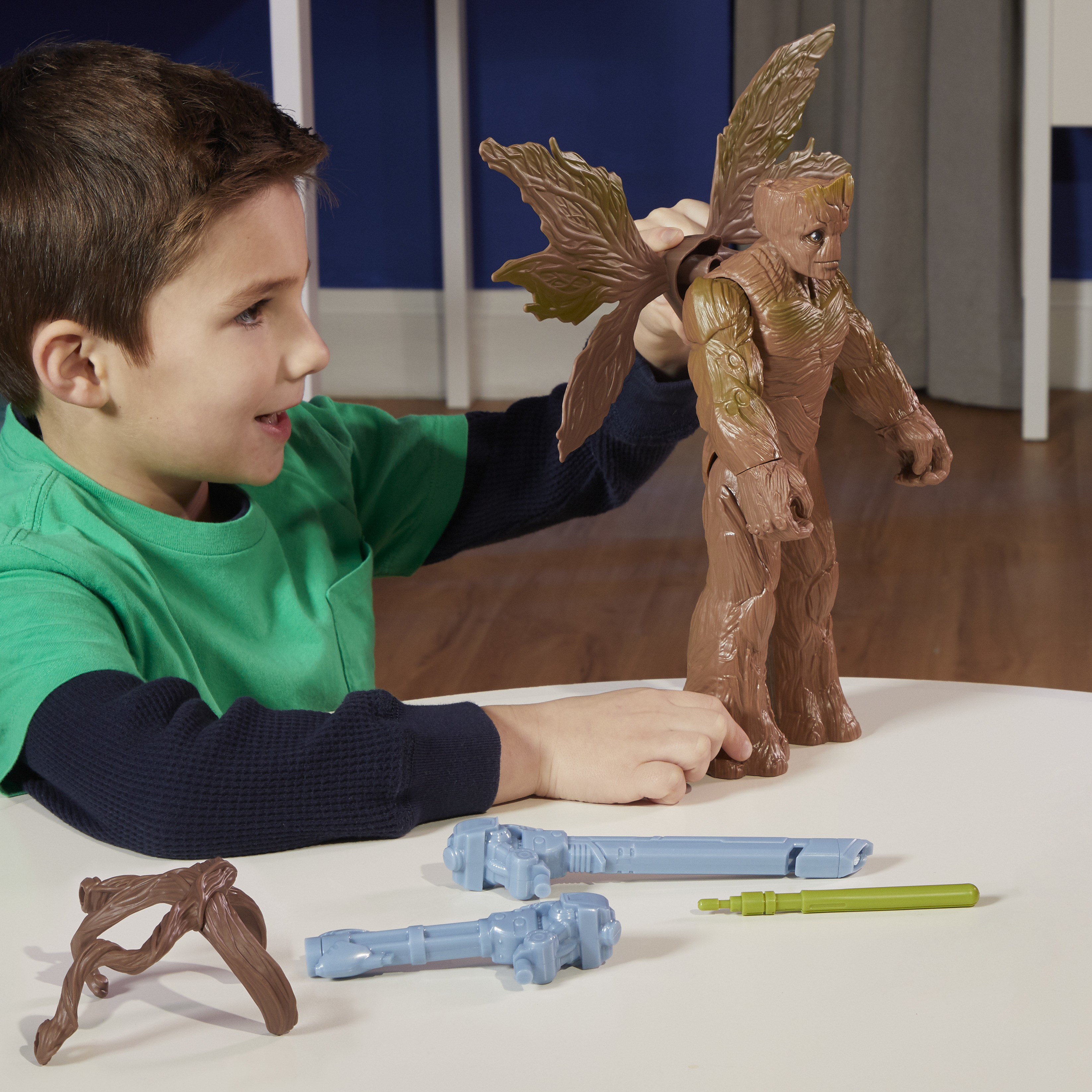 Un niño sostiene un juguete de Groot. Hay otros juguetes y piezas en la mesa. El fondo es azul.