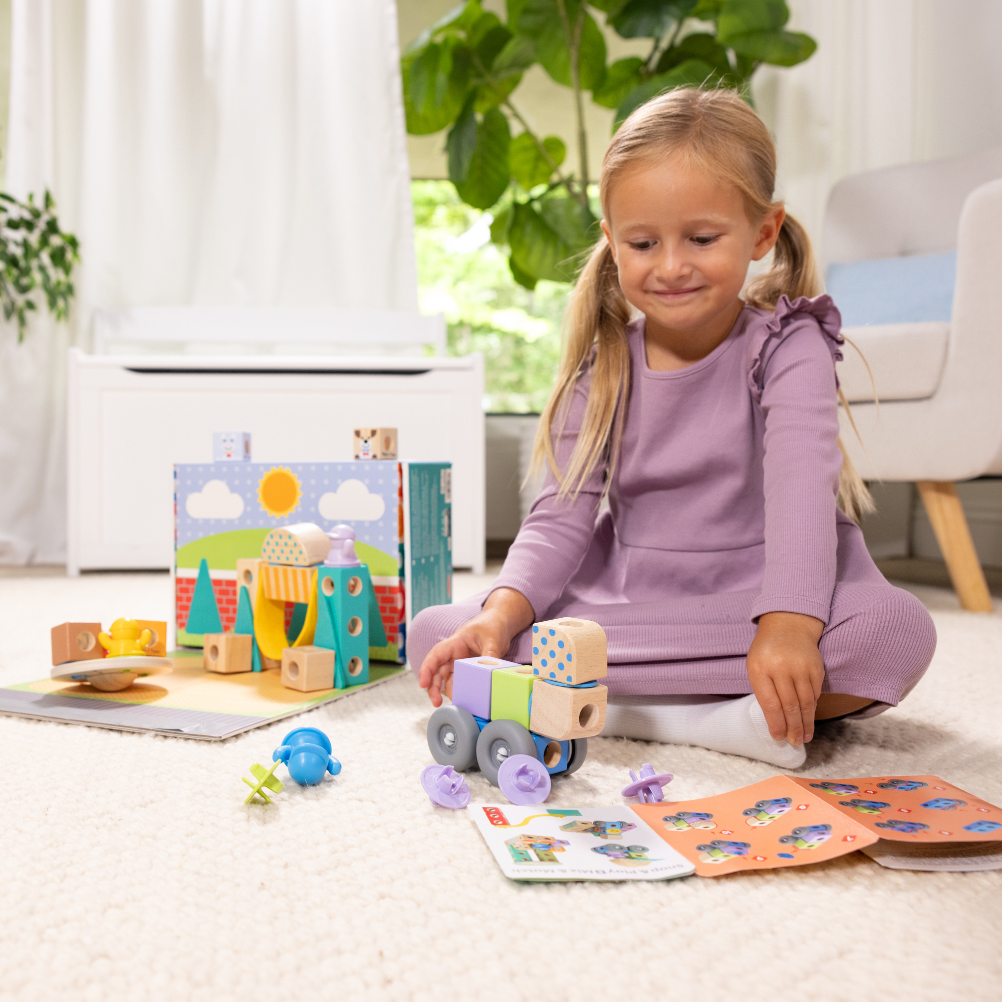 Una bambina gioca con blocchi di costruzione e un trenino su un tappeto. Vari giocattoli sono sparsi intorno a lei.