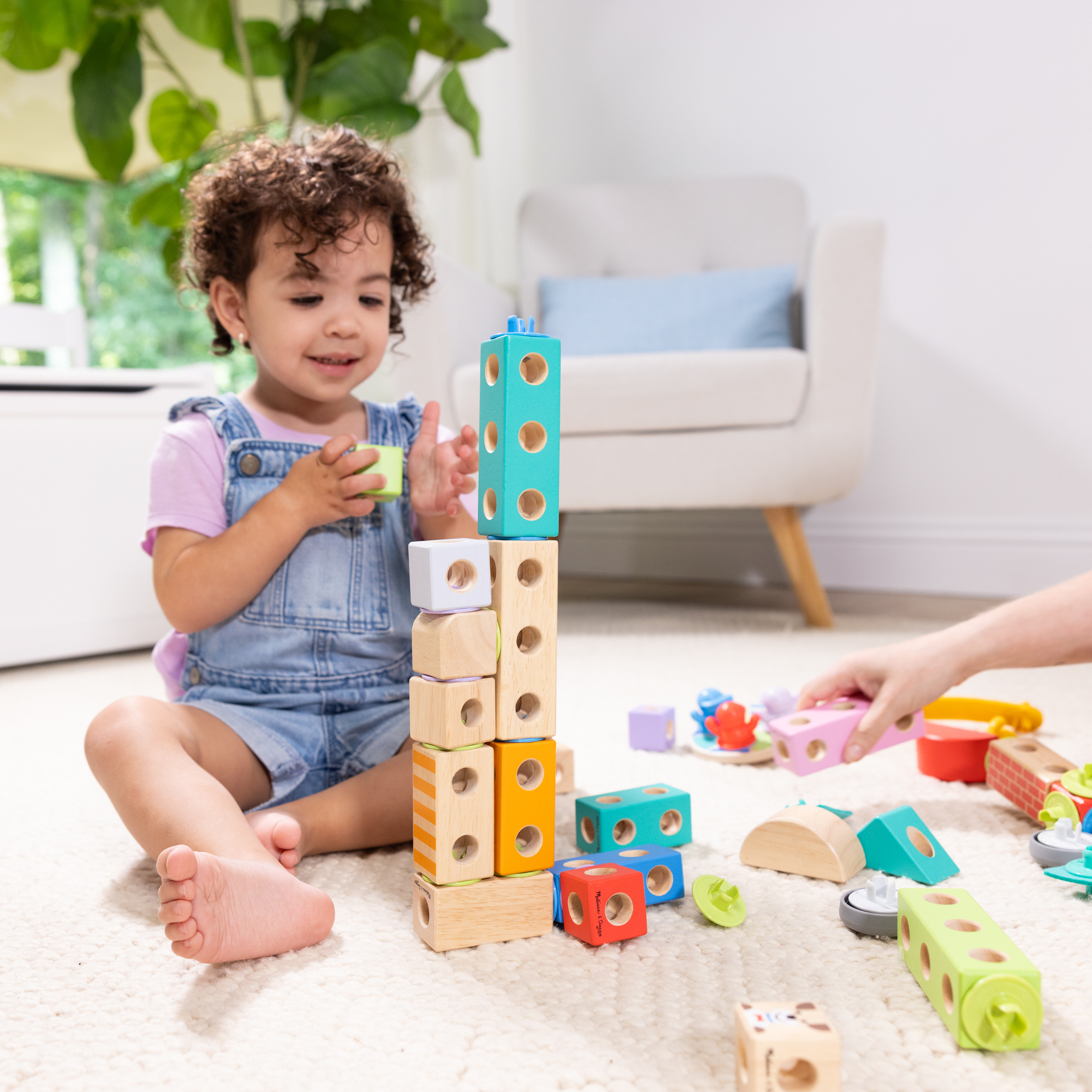 Una bambina gioca con blocchi di legno colorati. Viene costruita una torre di blocchi. Altri blocchi e giocattoli sono sul pavimento.