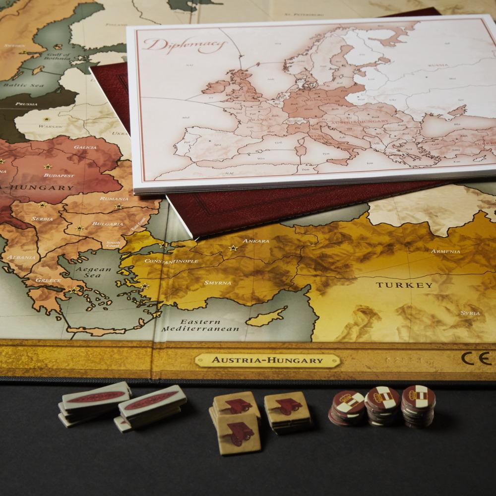 Un juego de mesa con mapas de Europa. Hay fichas y libros sobre la mesa. El juego se titula Diplomacia. Austria-Hungría es visible.