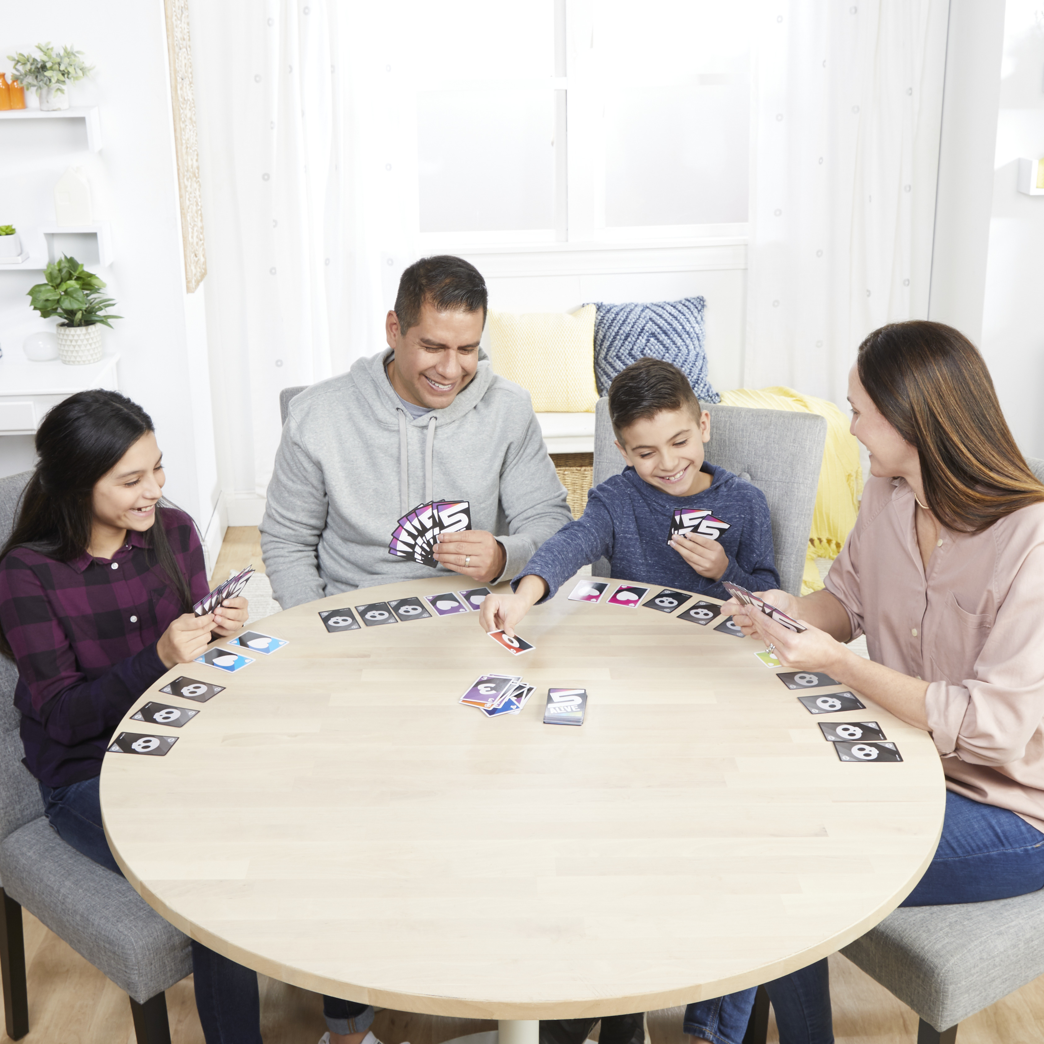 Familie spielt Kartenspiel. Sie sitzen an einem runden Tisch und lächeln. Karten sind sichtbar.