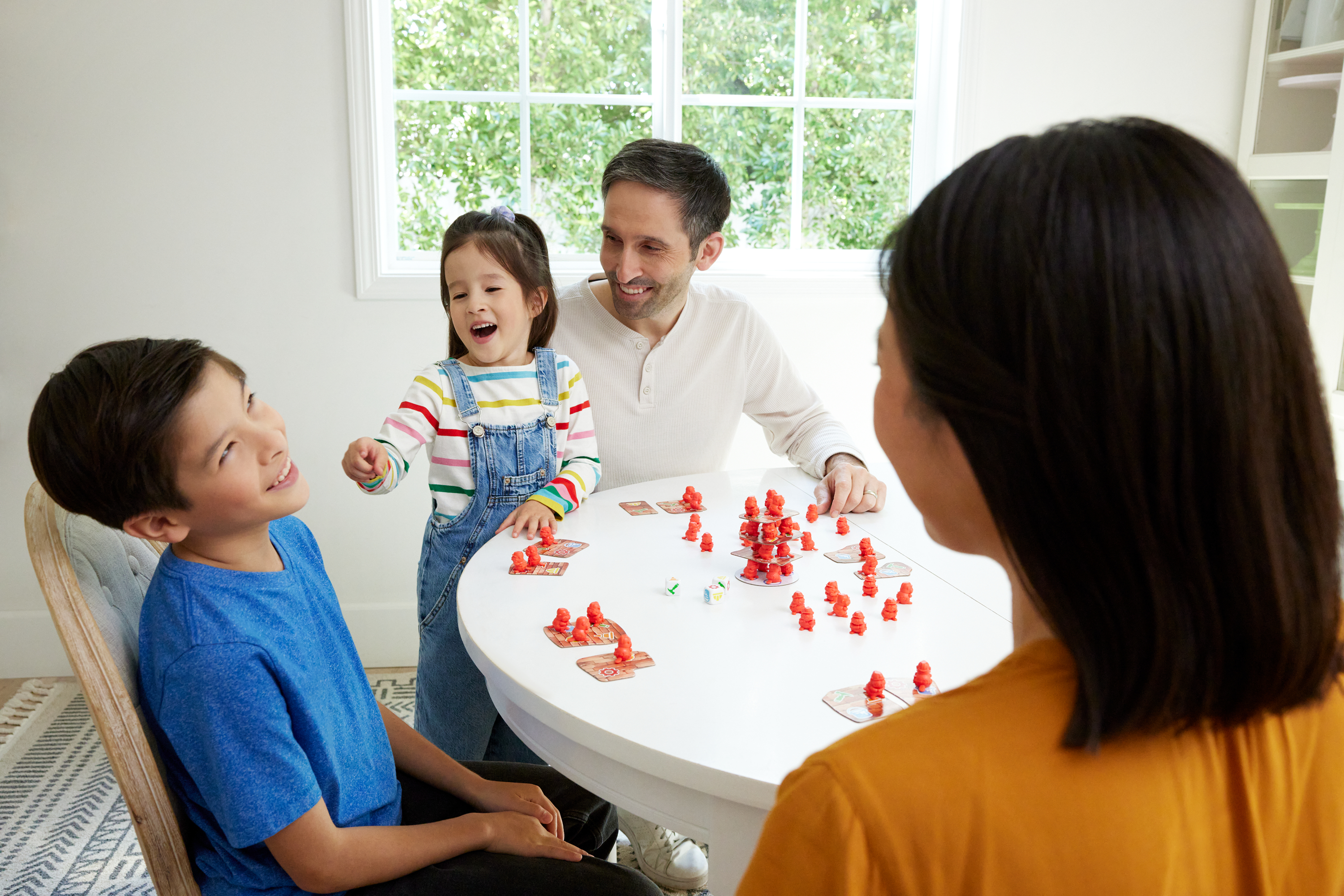 Famiglia che gioca a un gioco da tavolo su un tavolo rotondo. Le persone sorridono. Pezzi rossi del gioco sul tavolo.