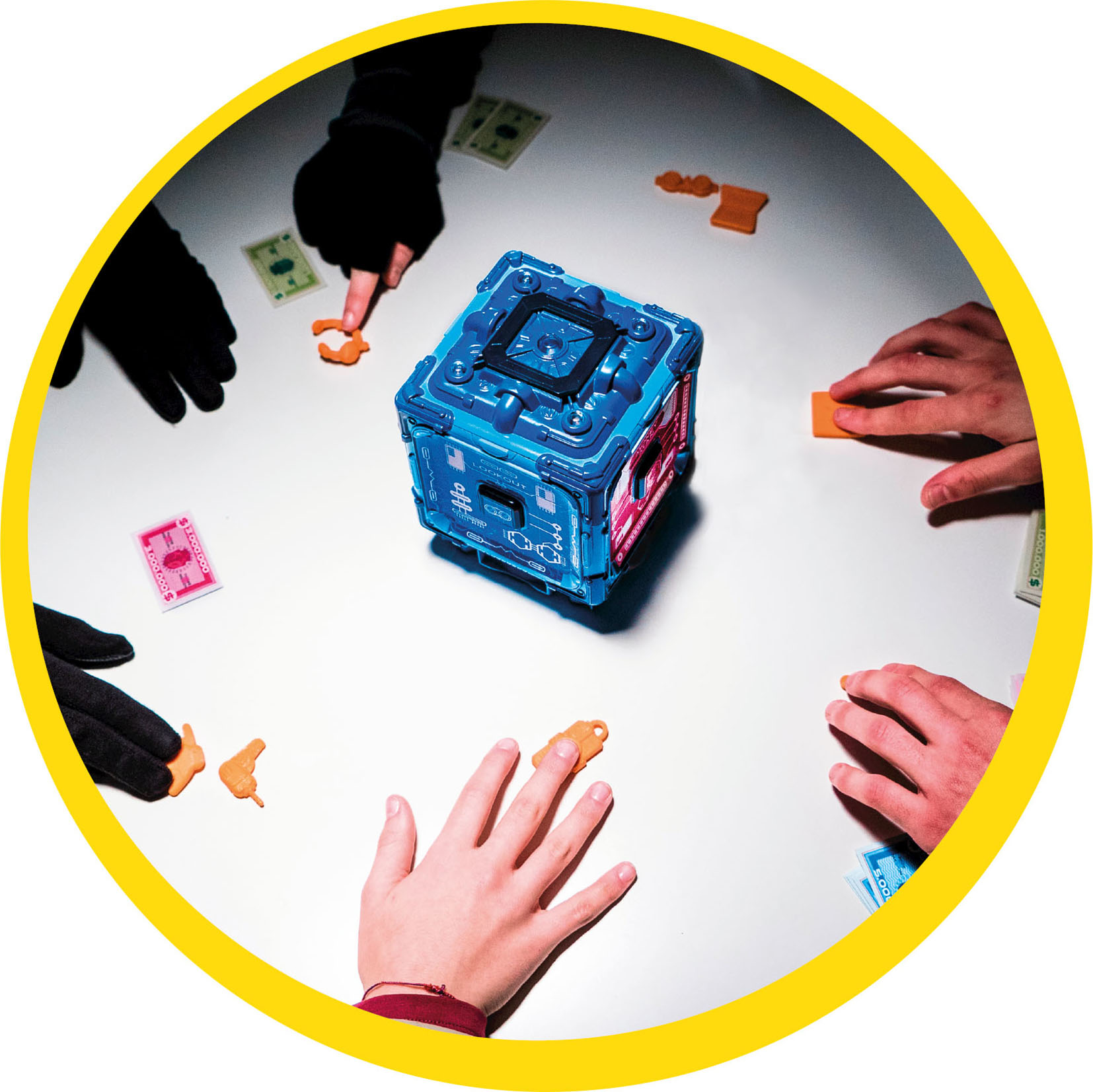 Hände um einen blauen Würfel. Kleine orangefarbene Spielsteine und Spielgeld sind verstreut.