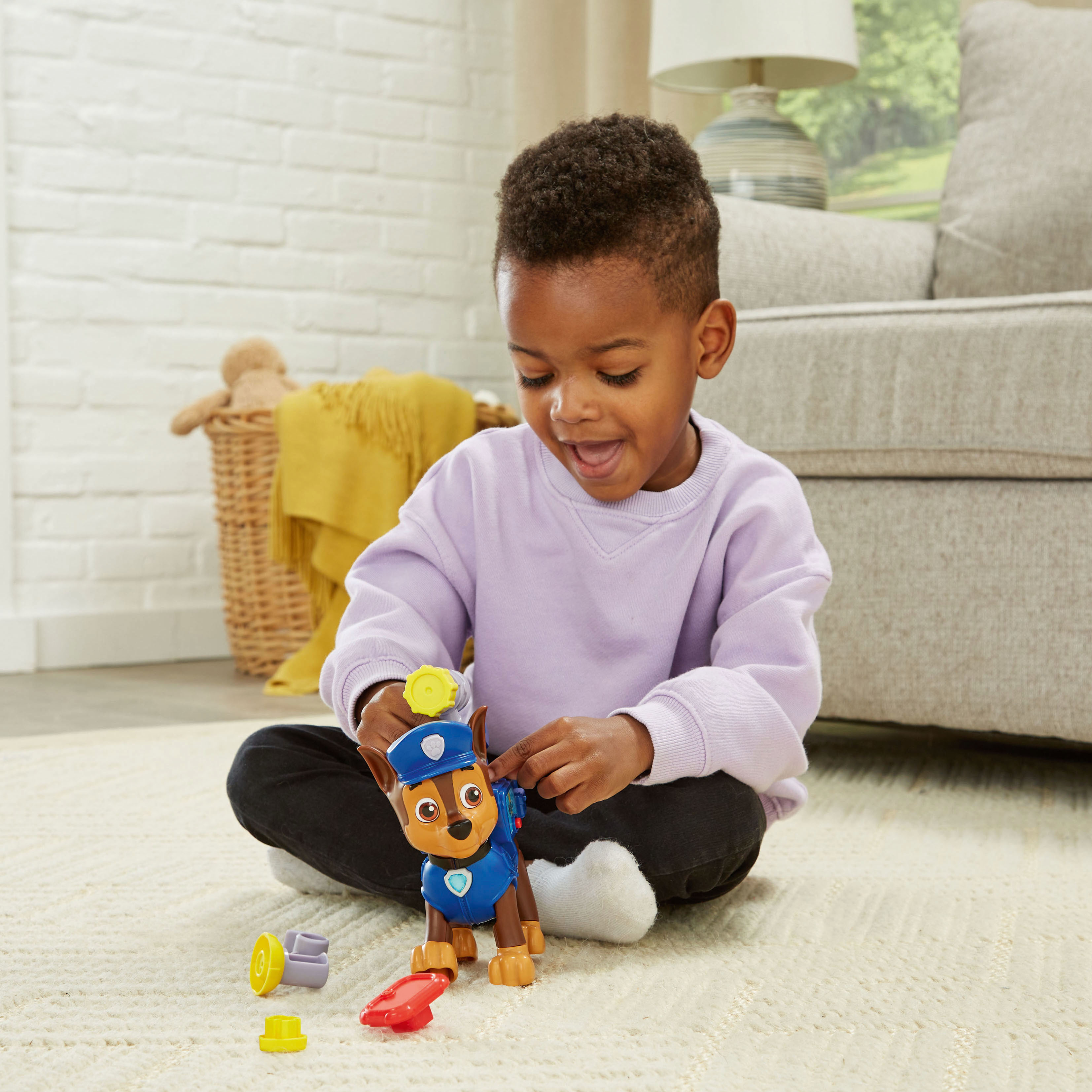 Un bambino gioca con un giocattolo di Paw Patrol. Il ragazzo sorride. Giocattoli e coperta sullo sfondo.