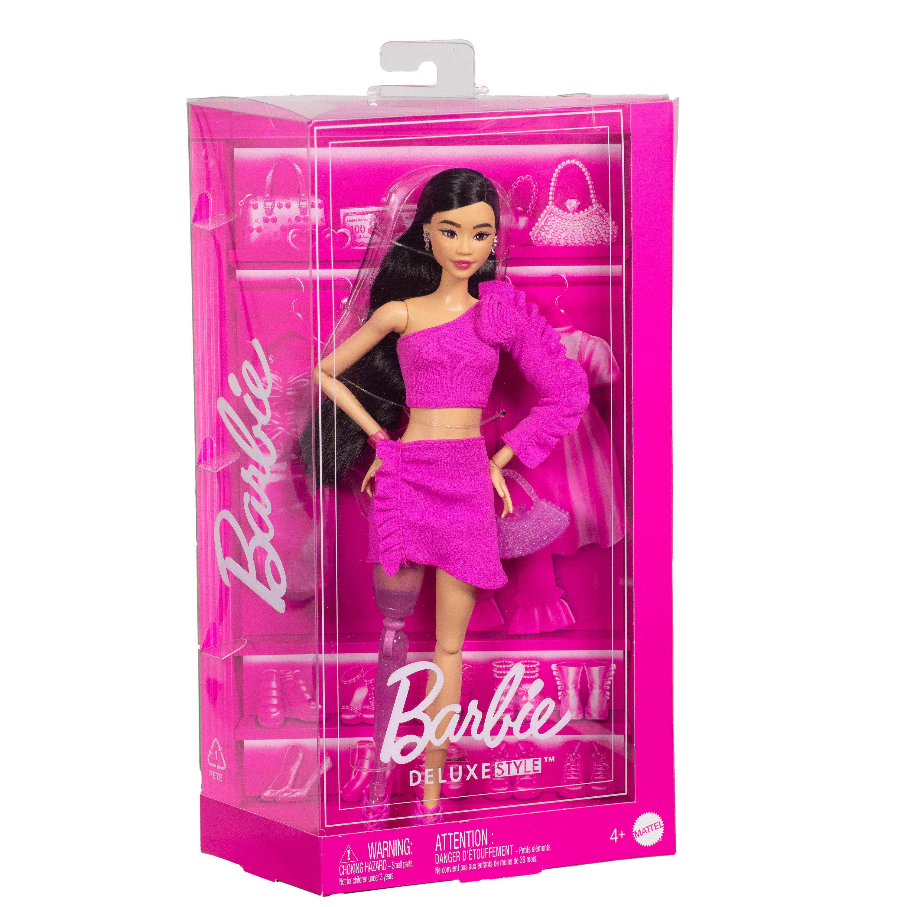 Eine Barbie-Puppe in einem rosa Outfit befindet sich in einer rosa Box. Die Puppe hat schwarzes Haar und trägt einen Rock.