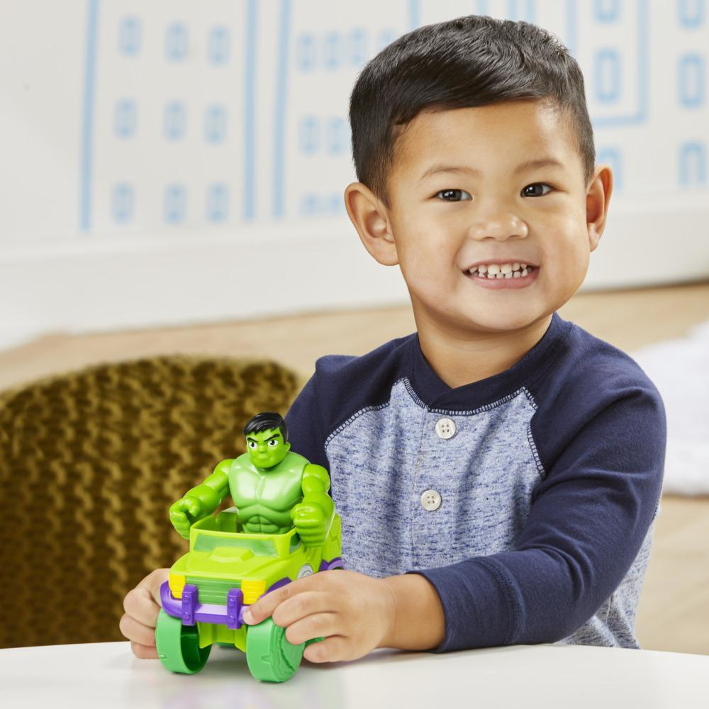 Ein lächelnder Junge hält ein Hulk-Spielzeugauto. Das Spielzeug ist grün und lila. Der Junge trägt ein blaues und graues Hemd.