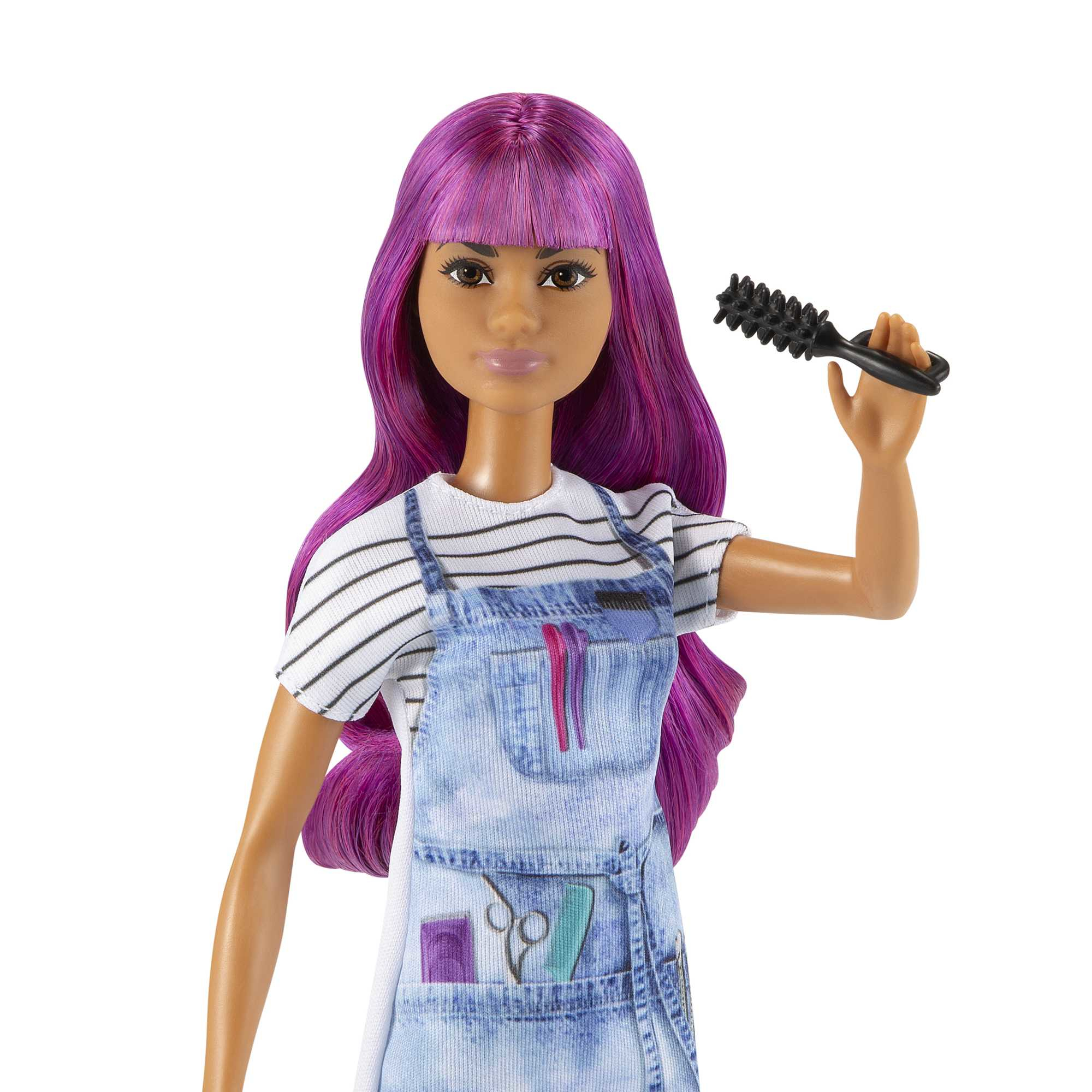 Eine Puppe mit lila Haaren, die eine Jeansschürze trägt, hält eine schwarze Haarbürste. Die Puppe steht vor weißem Hintergrund.