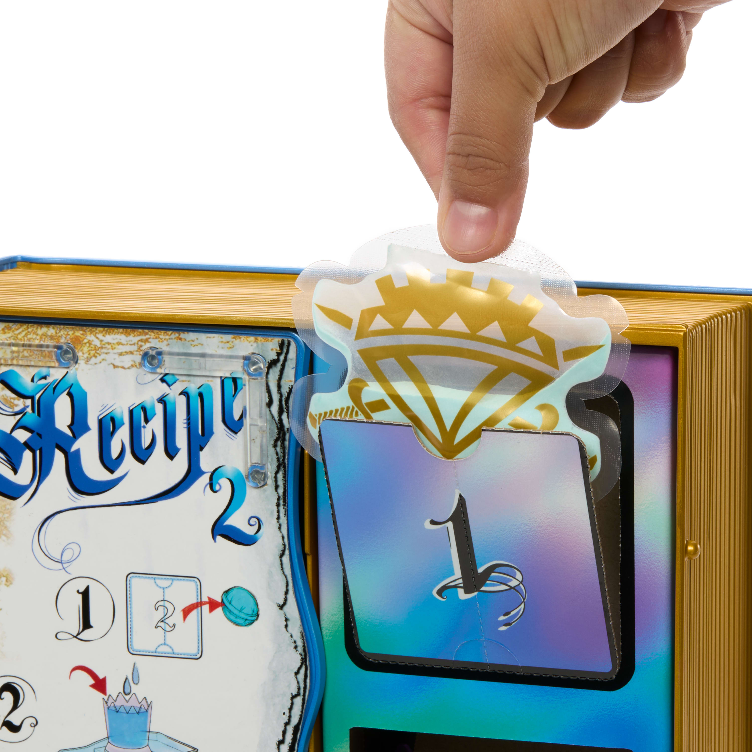 Ręka wyciąga naklejkę z książki-zabawki. Naklejka ma wzór diamentu. Książka jest niebieska i złota.