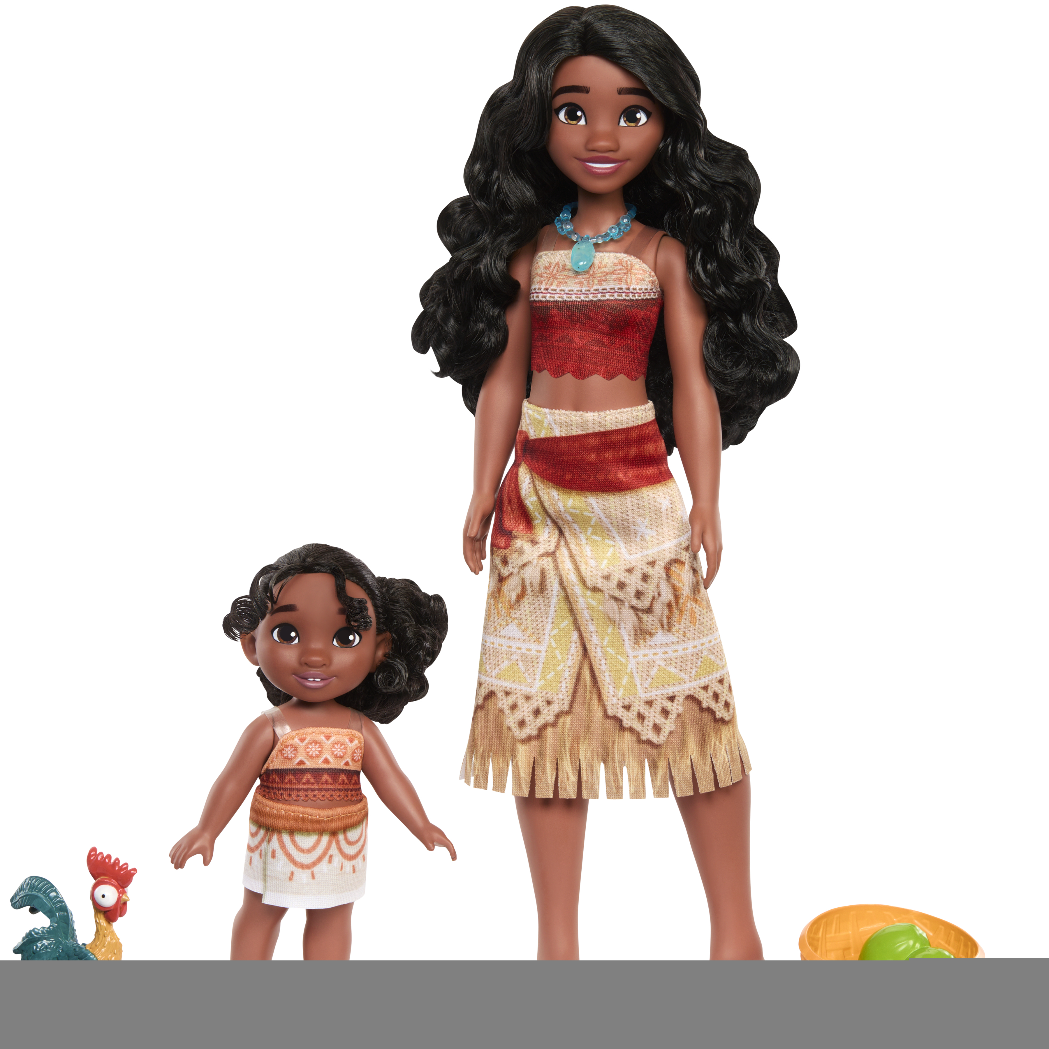 Dwie lalki Moana stoją, jedna duża i jedna mała. Kogut i kosz z zielonymi przedmiotami leżą na ziemi.