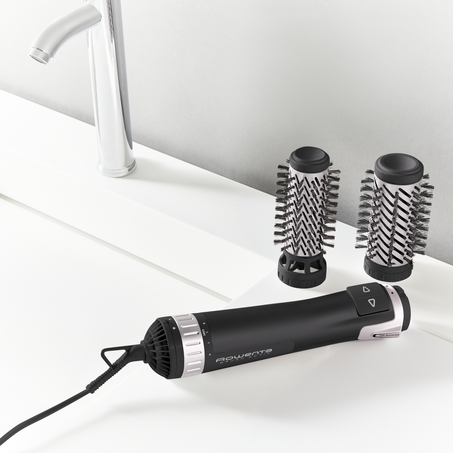 Uno strumento nero per lo styling dei capelli con attacchi a spazzola, un rubinetto cromato e una superficie bianca. Lo strumento ha il marchio Rowenta.