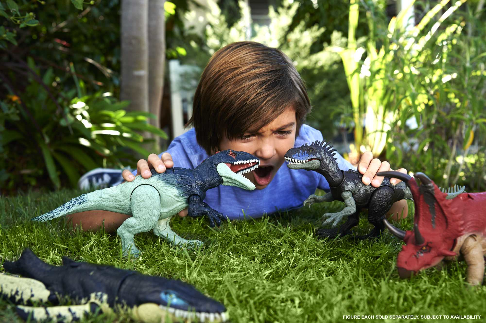 Un niño mira dinosaurios de juguete sobre hierba. Dos dinosaurios se enfrentan. Hay otros juguetes cerca. El niño está emocionado.