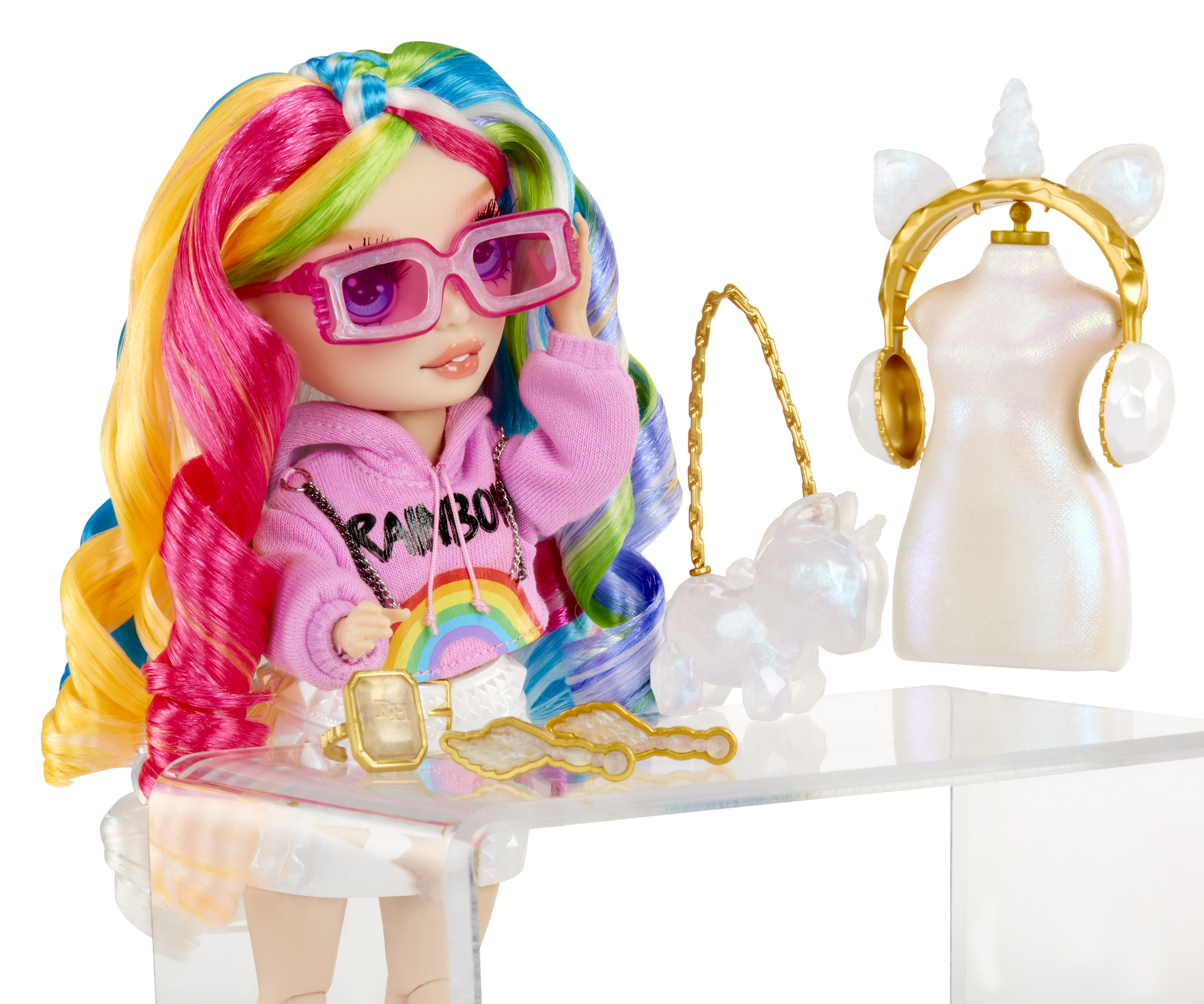 Lalka z tęczowymi włosami i różowymi okularami, w bluzie z kapturem. Akcesoria: torebka i biżuteria. Ekspozycja z motywem jednorożca.