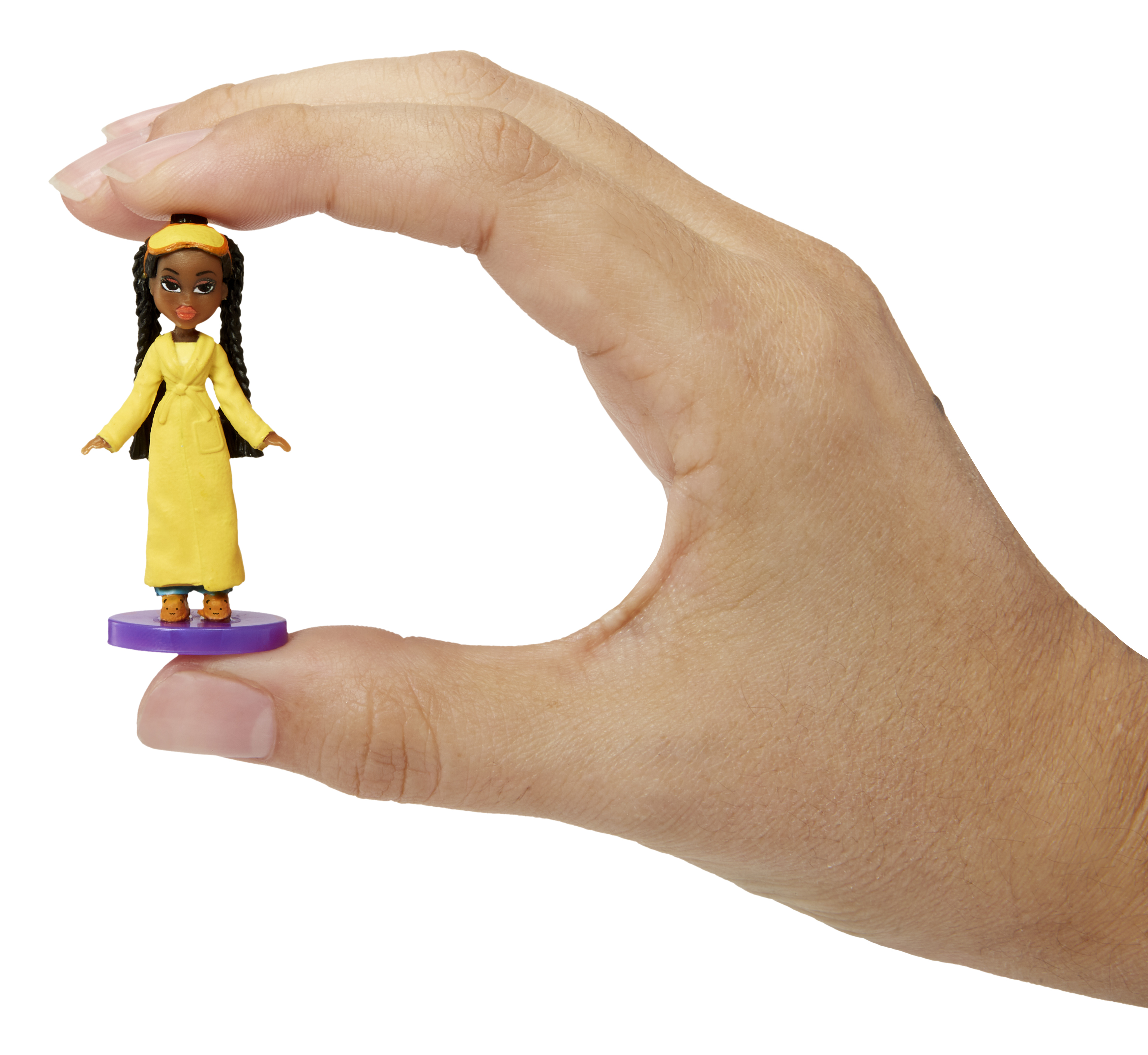 Ręka trzyma lalkę kobiety w żółtym płaszczu, stojącą na fioletowej podstawie. Tło jest białe.