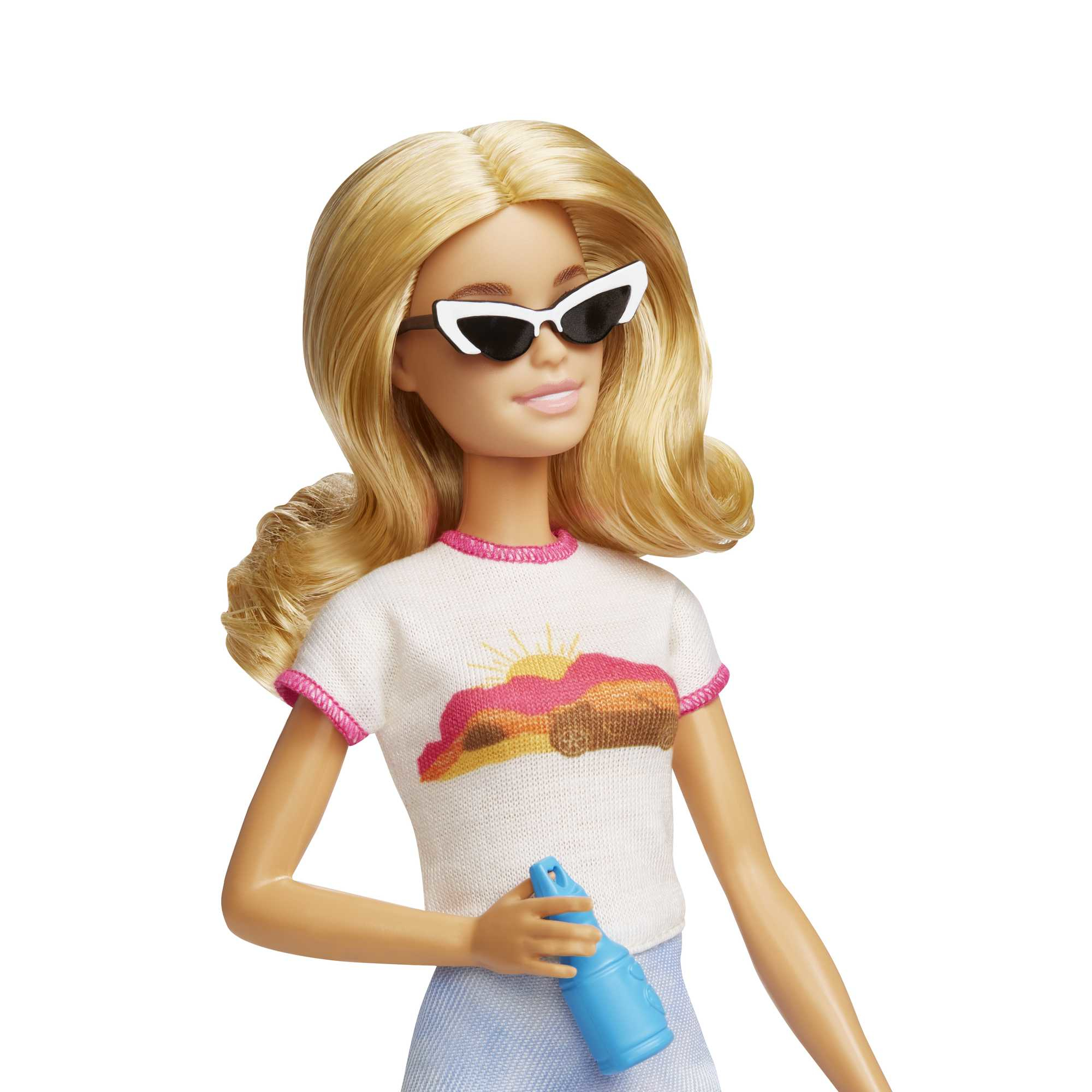 Muñeca Barbie rubia con gafas de sol, camiseta blanca con diseño de atardecer y sosteniendo un pulverizador azul.