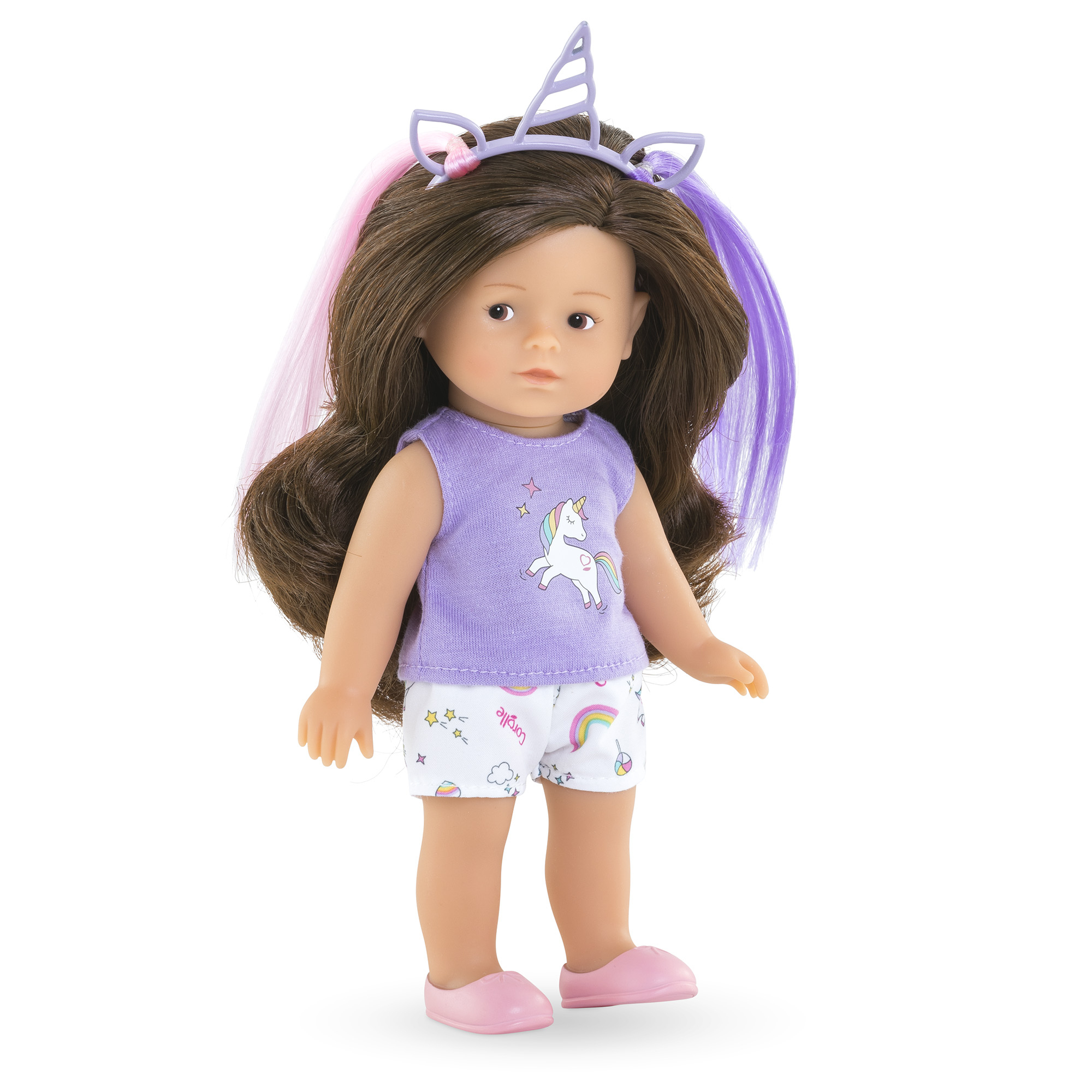 Eine Puppe mit braunen Haaren, einem Einhorn-Stirnband, lila Oberteil, weißen Shorts und rosa Schuhen steht auf weißem Hintergrund.