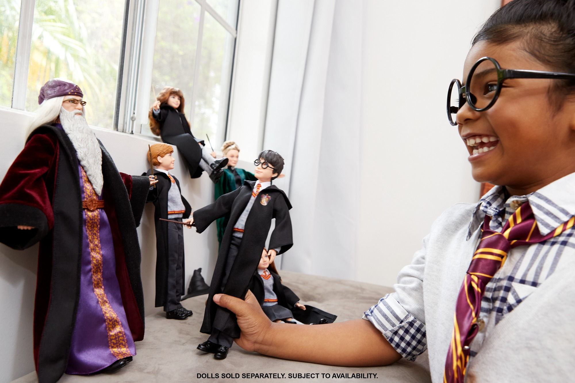 Una ragazza sorride, indossa occhiali, tiene in mano una bambola di Harry Potter. Altre bambole e una finestra sullo sfondo.