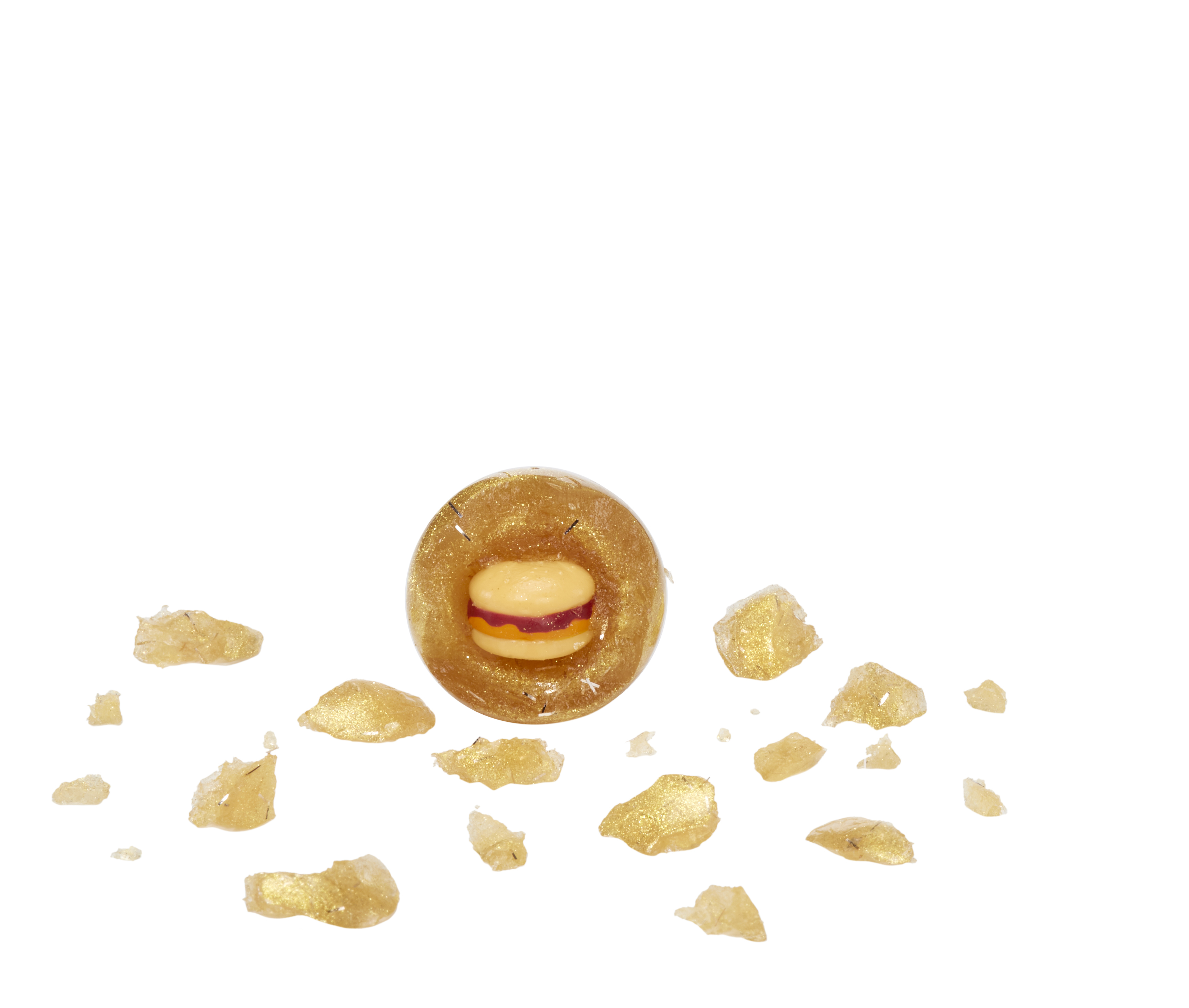 Złoty, pierścieniowaty obiekt z małym burgerem w środku i złotymi odłamkami rozsianymi na białym tle.