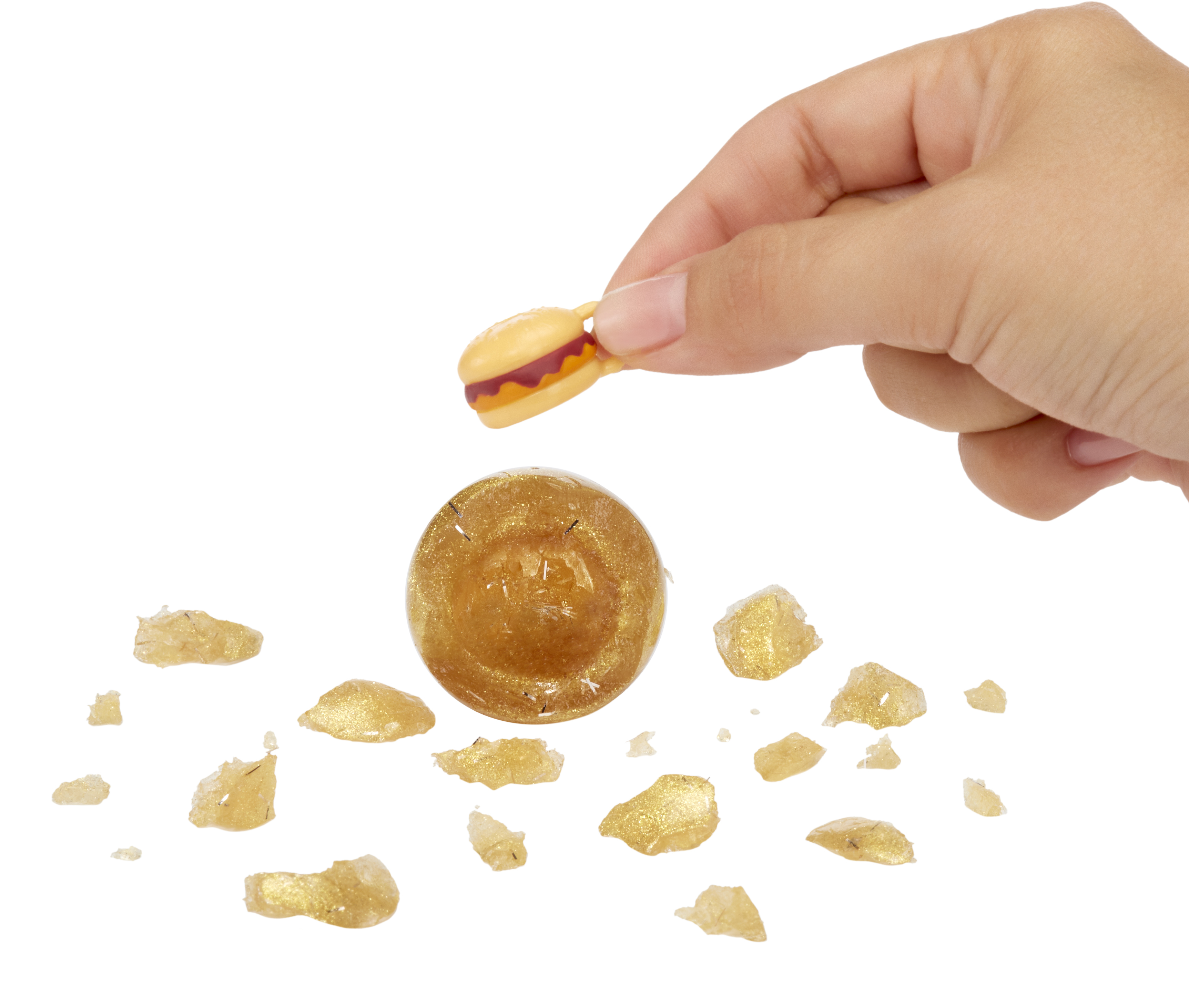Ręka trzyma zabawkowego burgera nad złotą kulą i rozrzuconymi złotymi odłamkami.