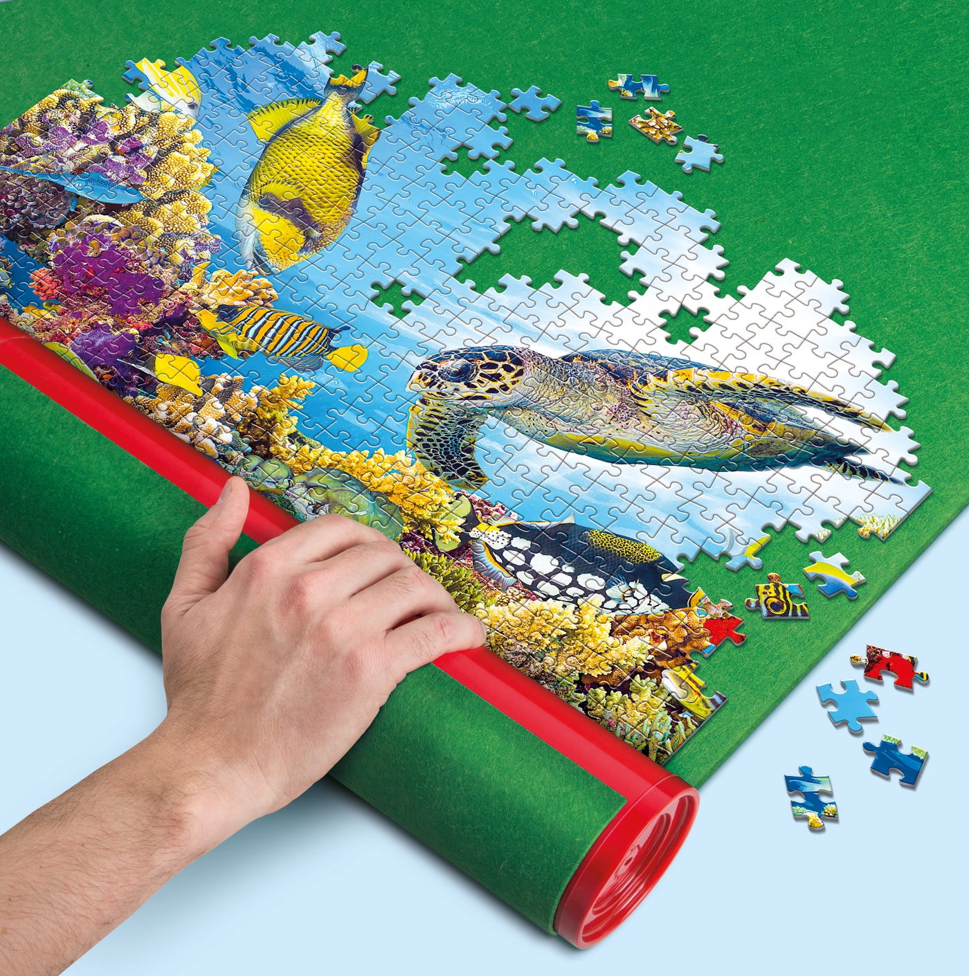 Eine Hand rollt eine Puzzlematte. Das teilweise zusammengesetzte Puzzle zeigt eine Meeresschildkröte, Fische und ein Korallenriff.